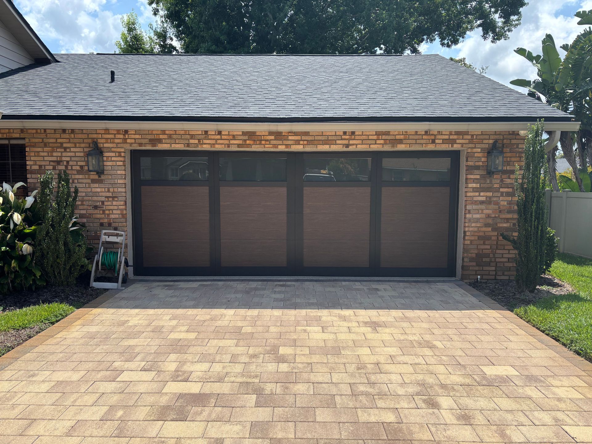 Brick garage with three dark doors and a paved driveway under a sunny sky