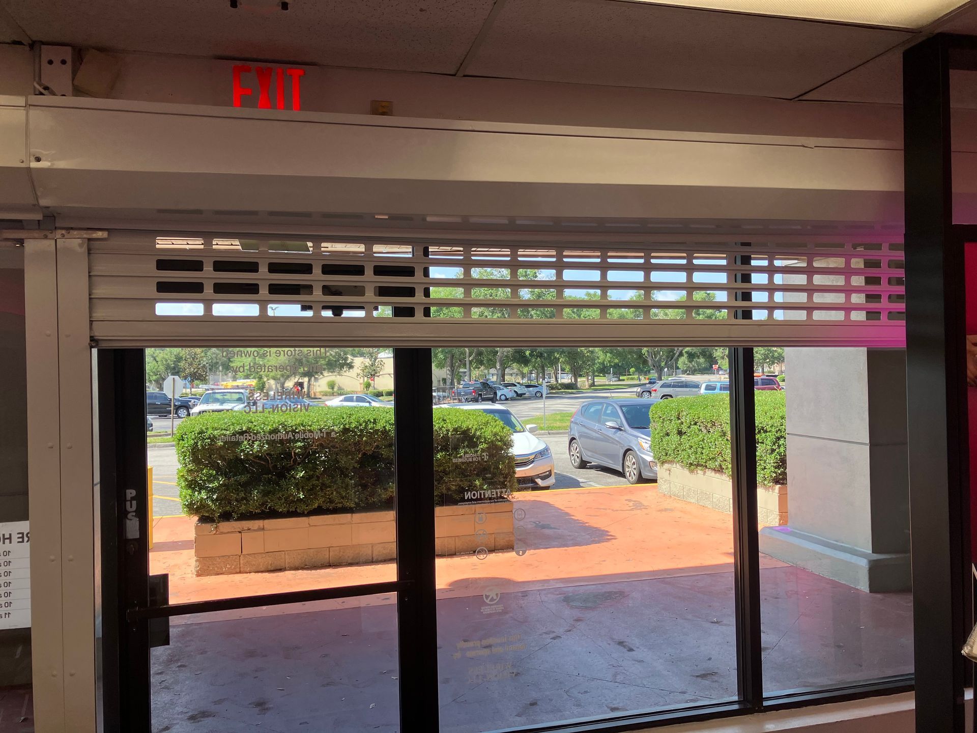 Sliding glass doors with white blinds, opening to a sunny patio and parked cars outside.