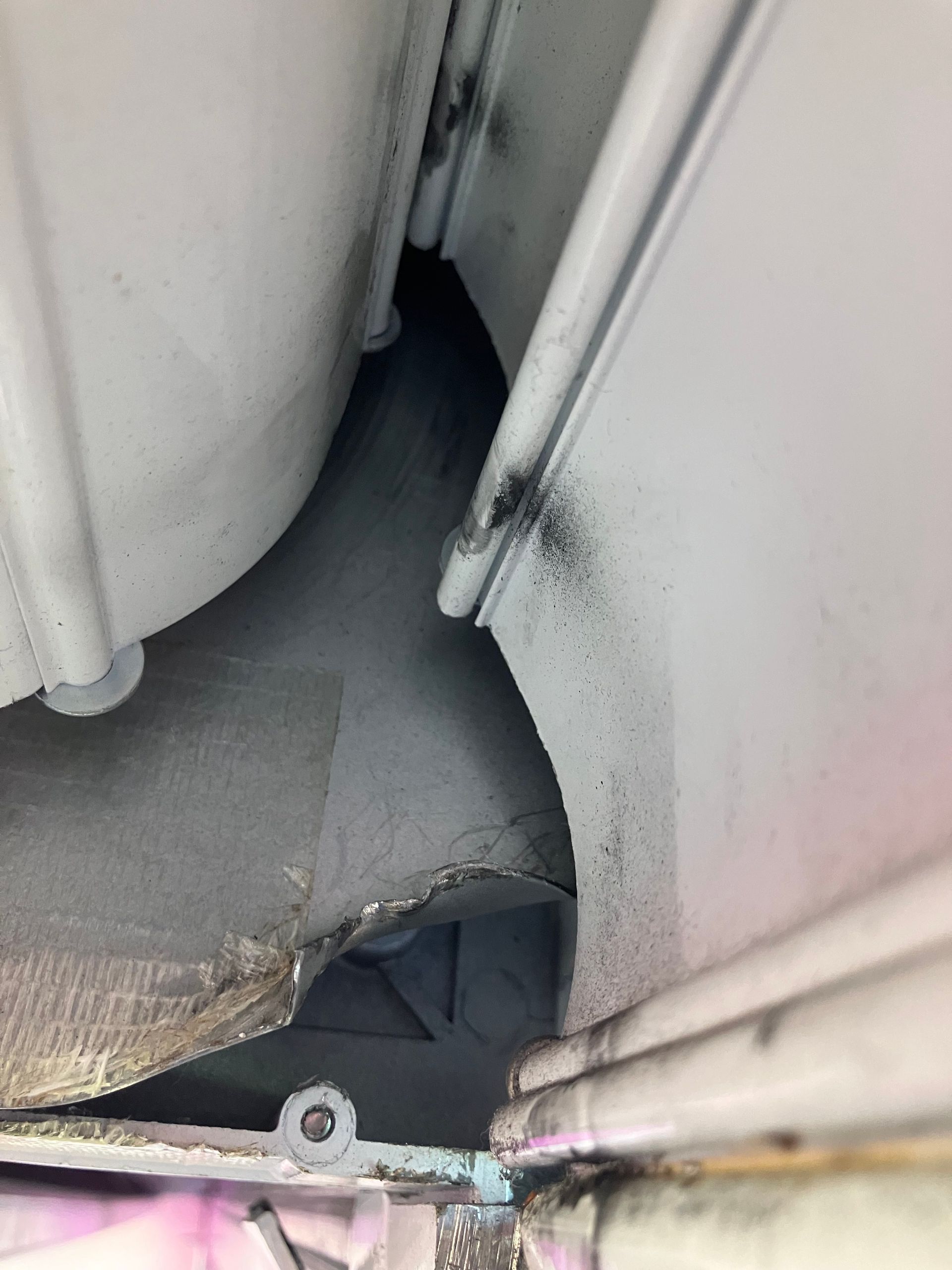 Close-up of a narrow gap between white panels with dark grime and a bent metal edge.