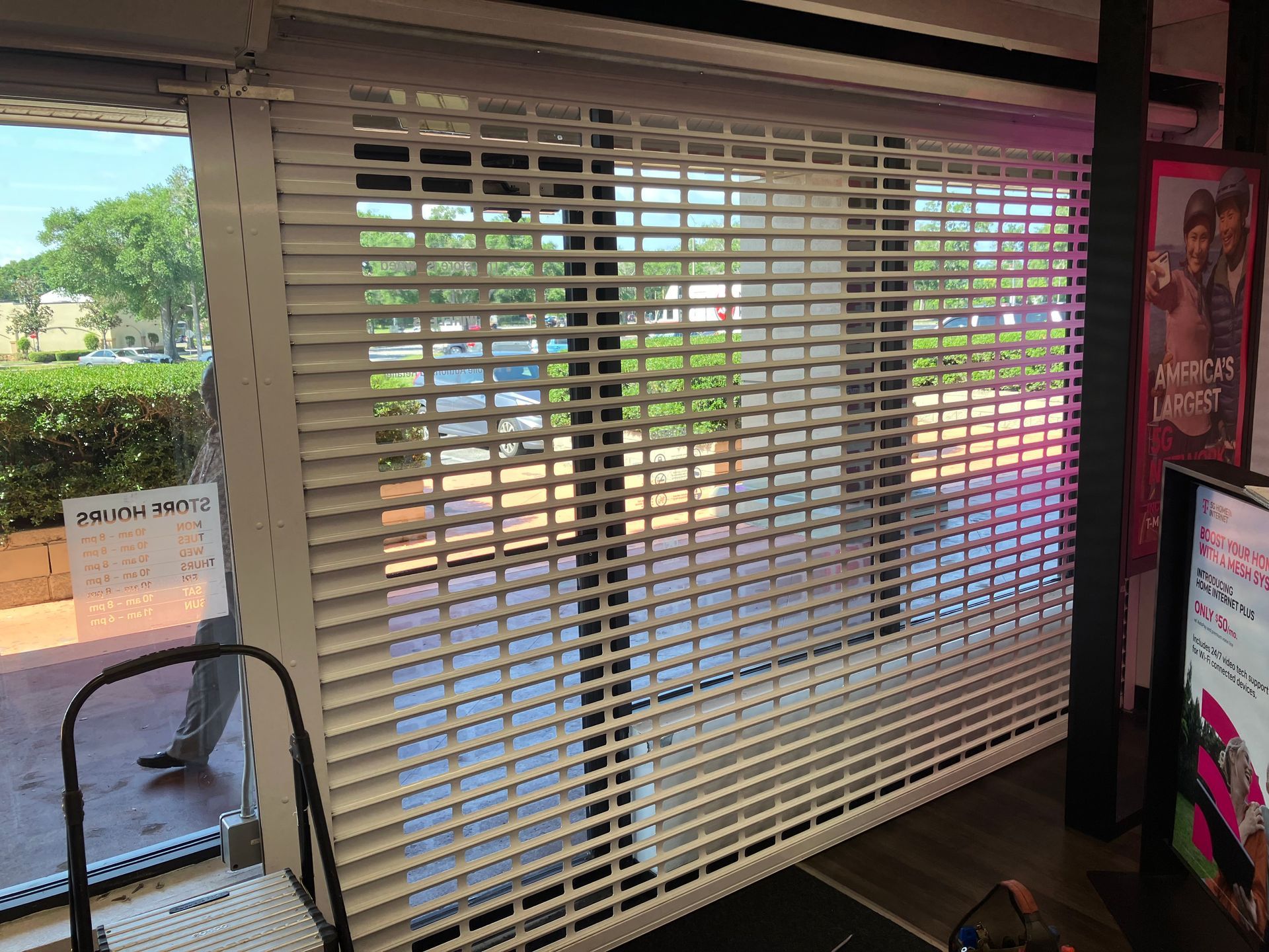Closed white blinds in a storefront window with a black chair and colorful posters on the right.