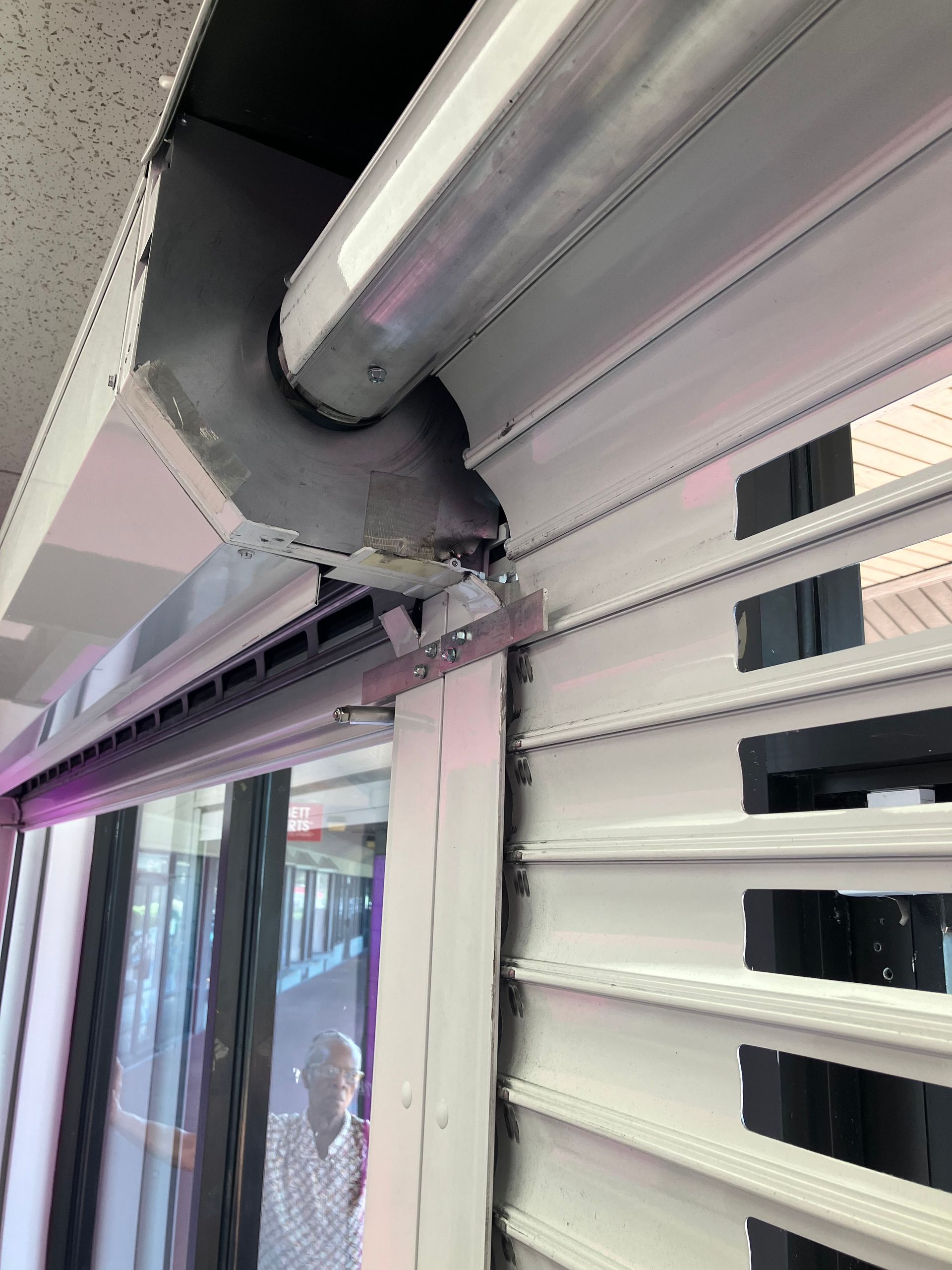 Close-up of a gray roller shutter track with a black cover and metal slats on a storefront facade