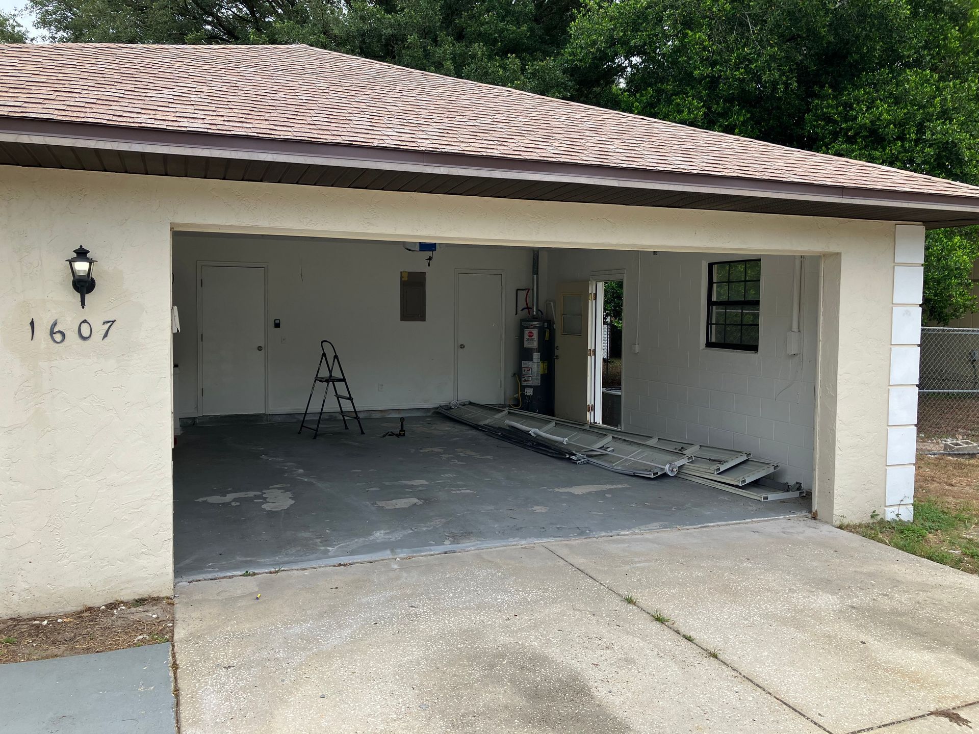 Garage with open door, white walls, and tools inside, beside a driveway and house number 1607.