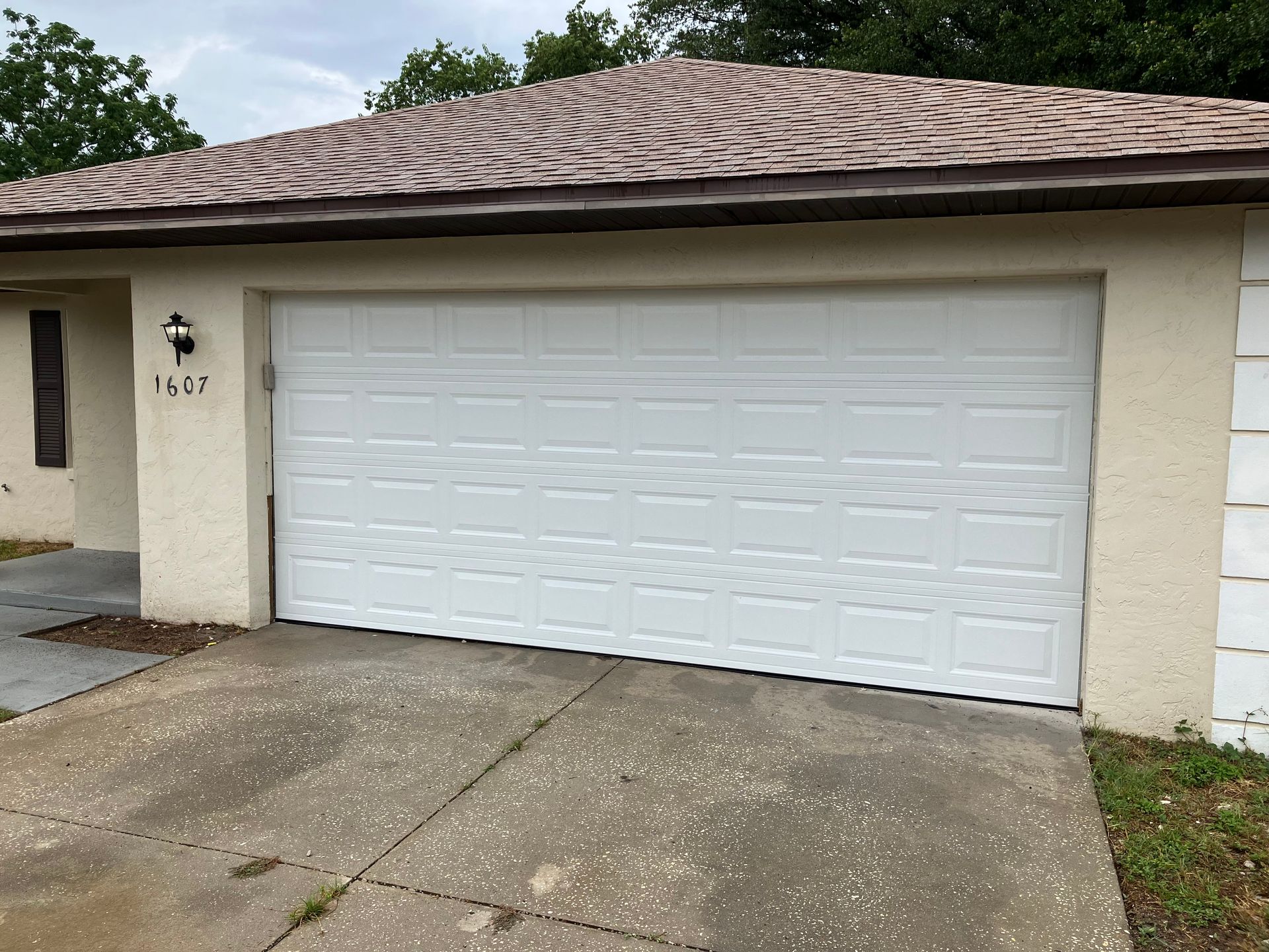White double garage door on a tan house with a concrete driveway and partial front entry visible