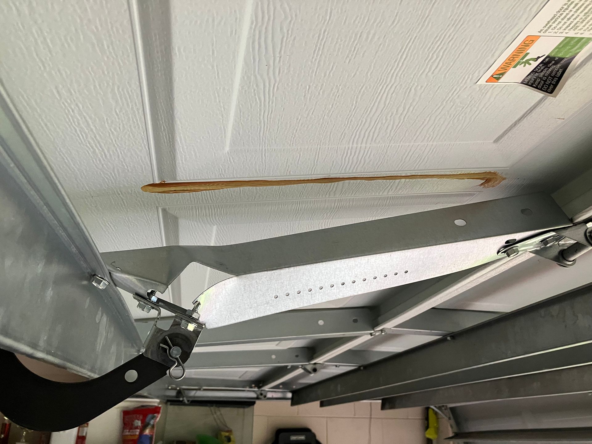 Inside a metal structure, a ceiling panel has a long crack or peel, with beams and hardware visible below.