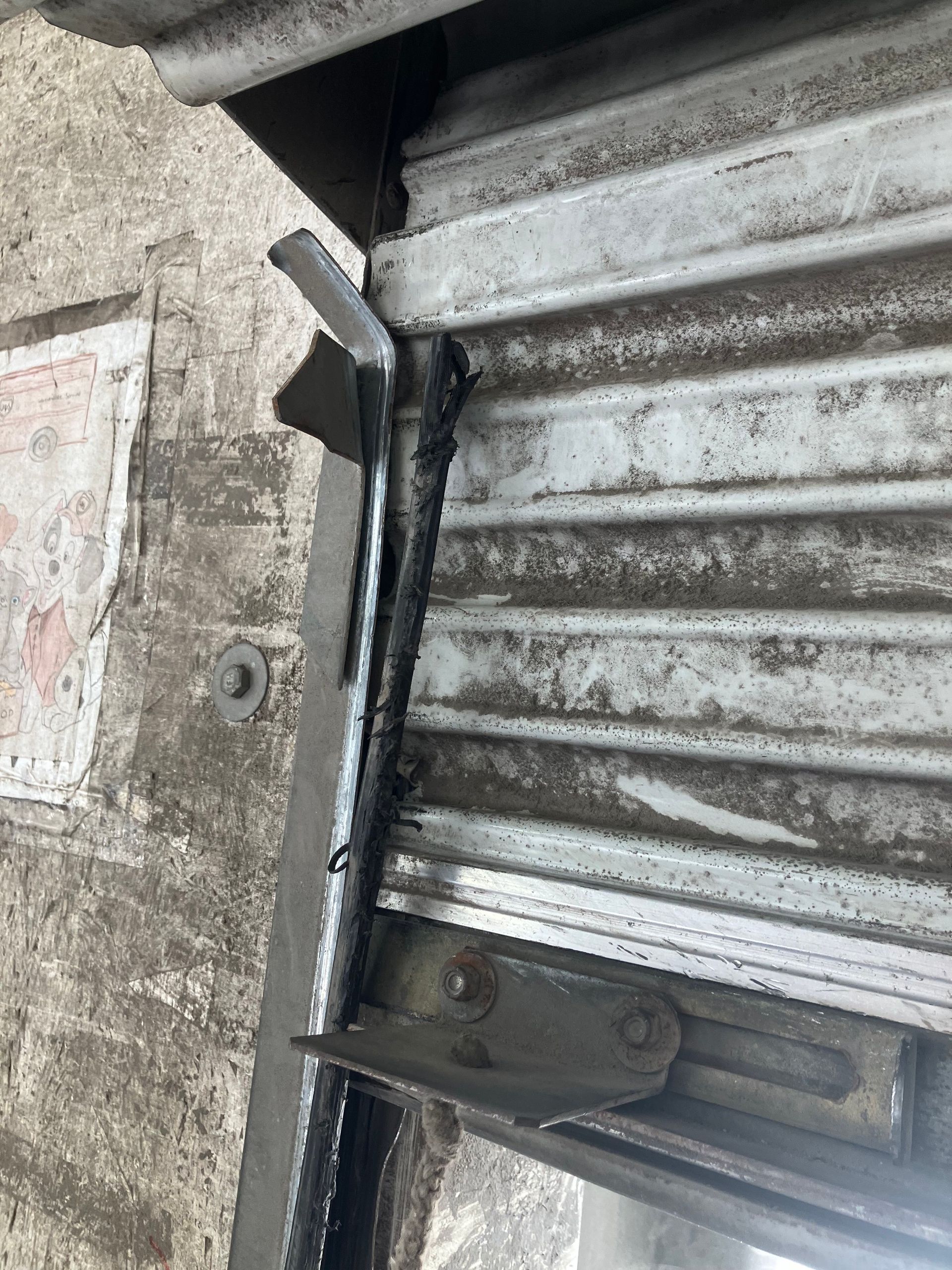 Close-up of a weathered metal roll-up door with a black latch and concrete wall beside it