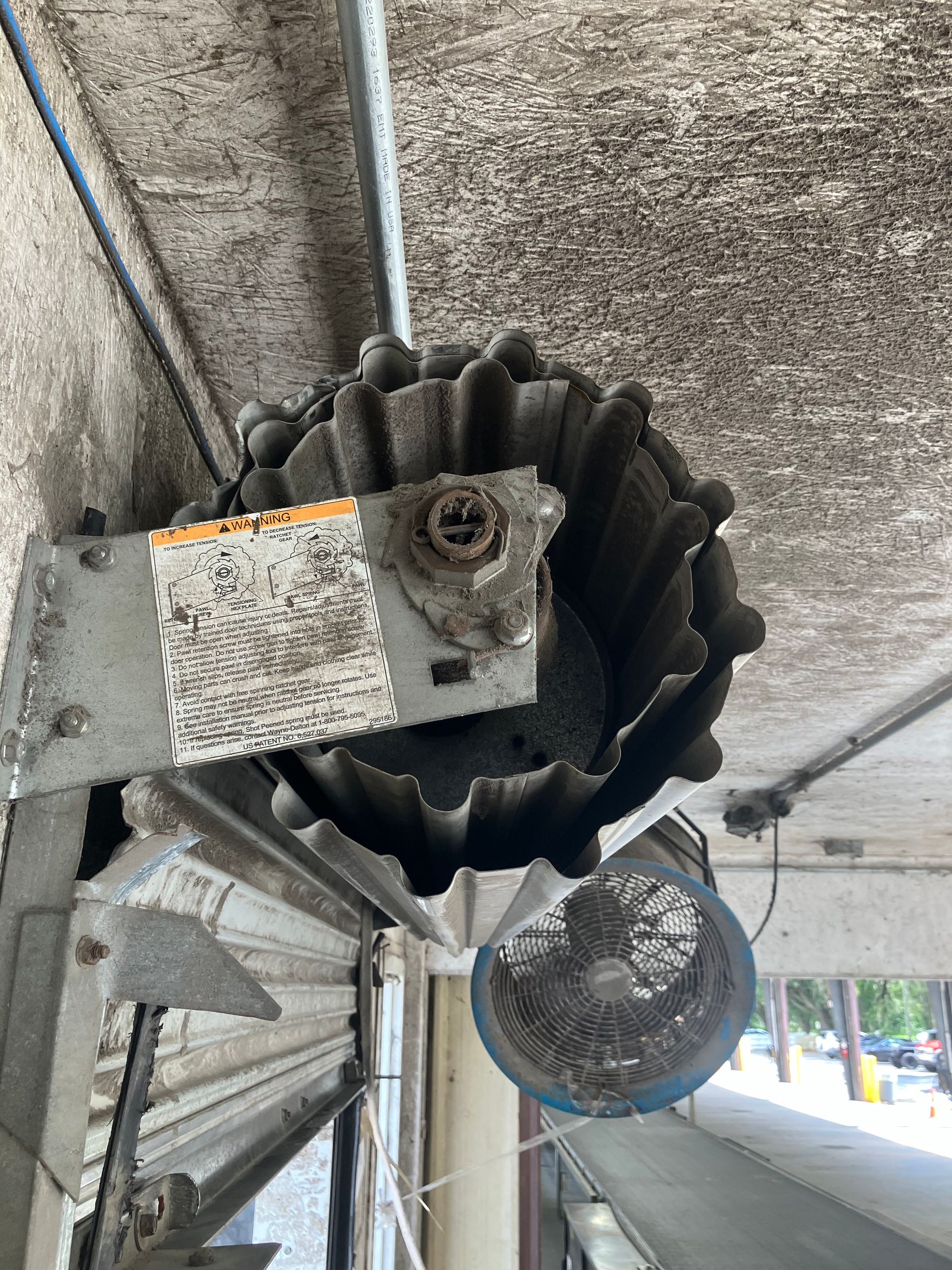 Industrial overhead fan with black rubber blades and a metal motor housing mounted near a concrete ceiling.