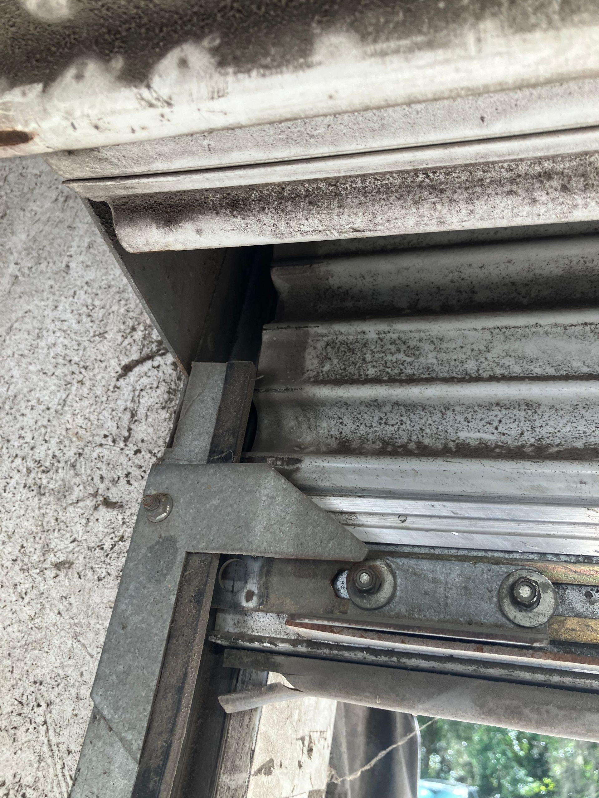 Close-up of a weathered metal window shutter hinge with rust and dust.