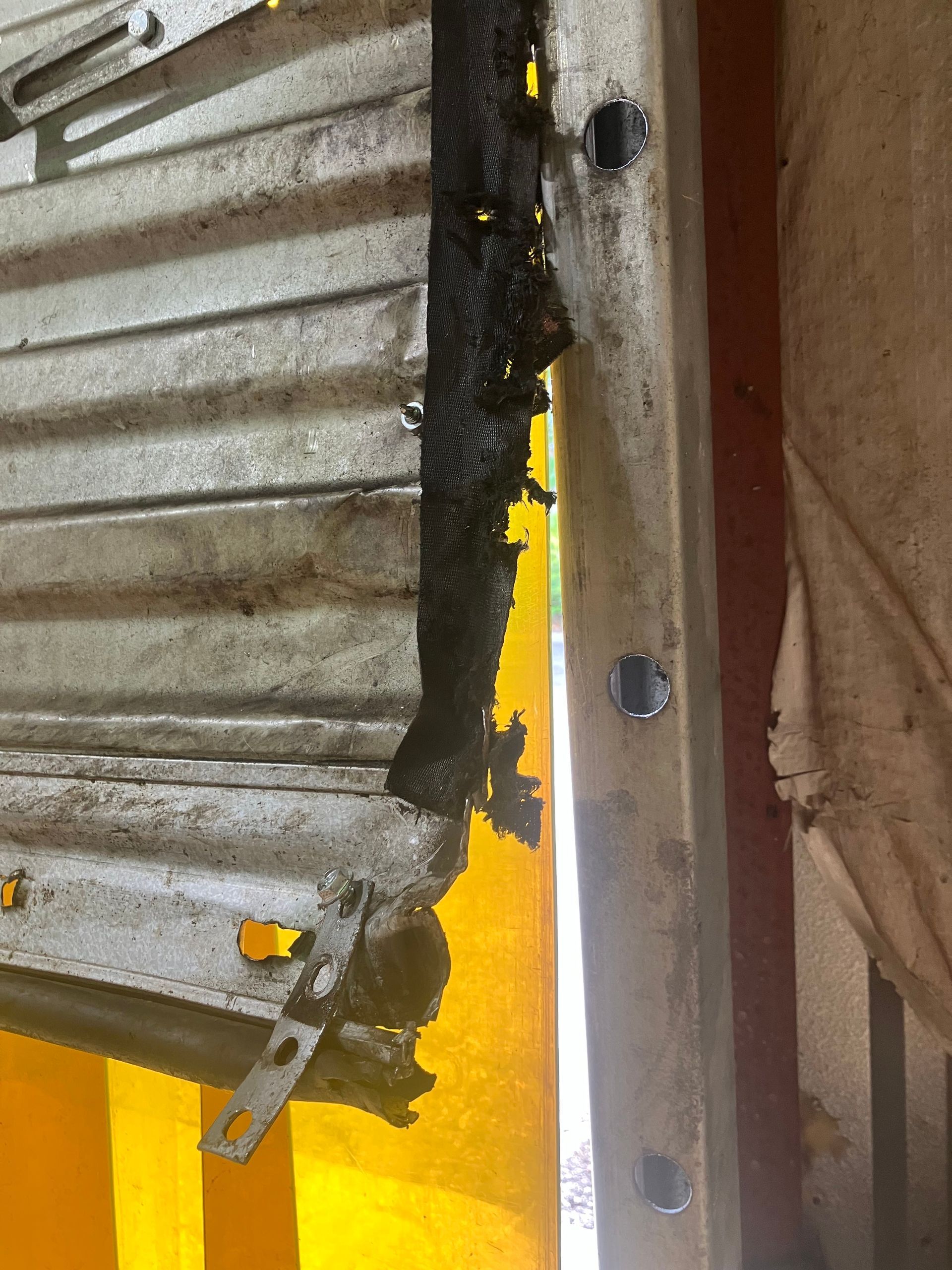 Close-up of a rusty corrugated metal panel beside a yellow wall and a vertical metal beam with bolts.