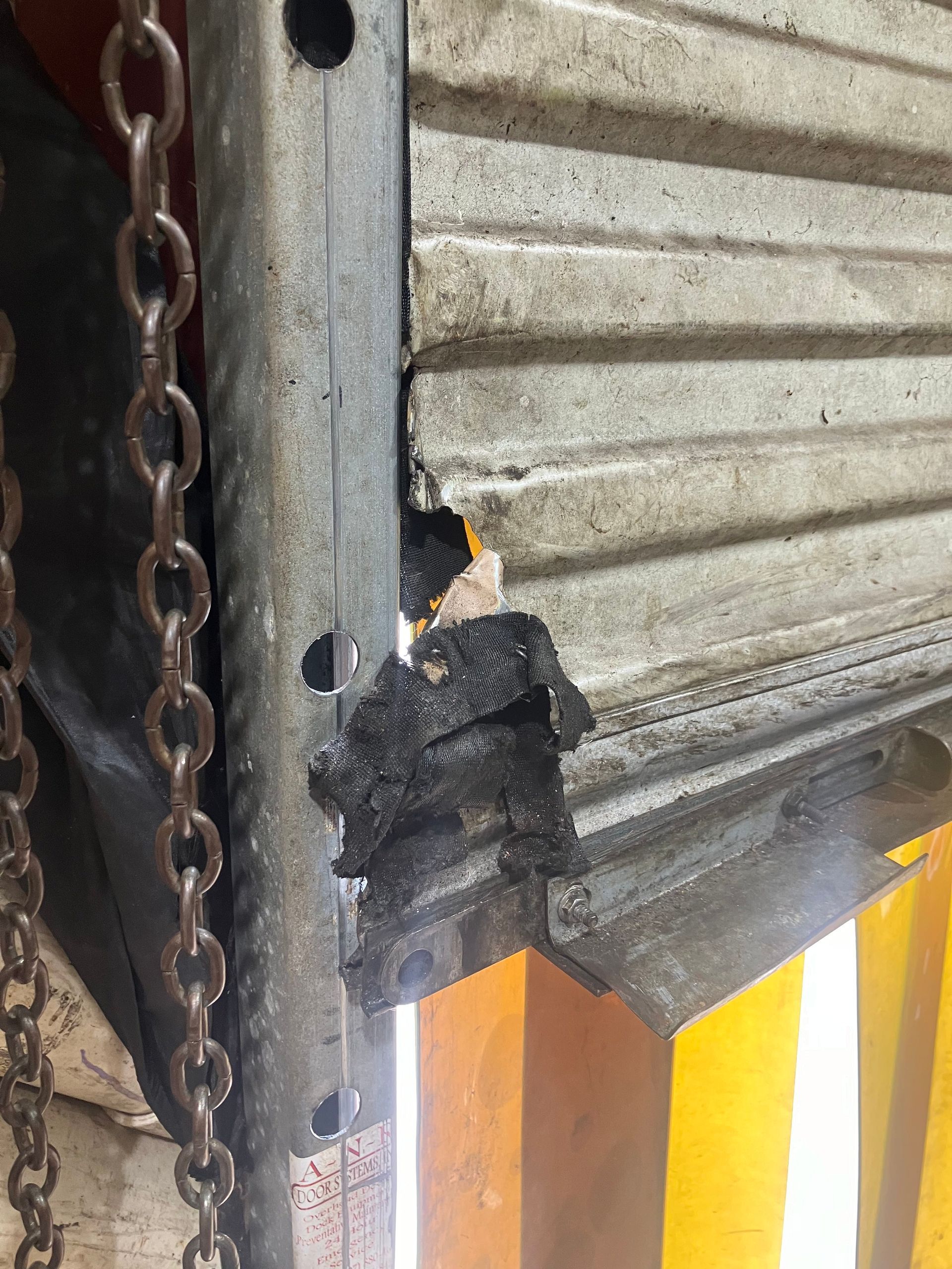 Damaged metal shutter edge beside a hanging chain, with a small bird perched on the broken corner.