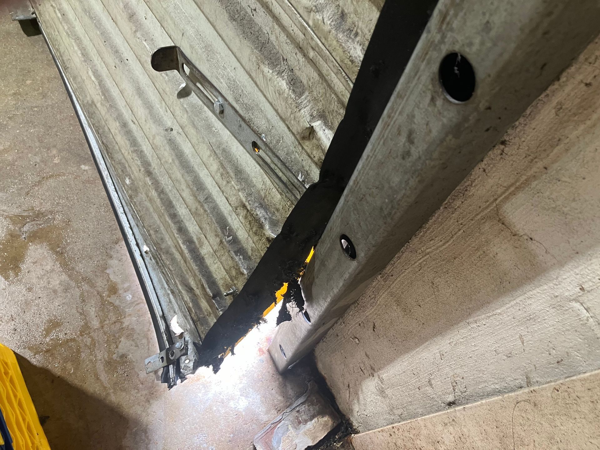 Damaged garage door panel bent open, revealing bright light and debris on a concrete floor.