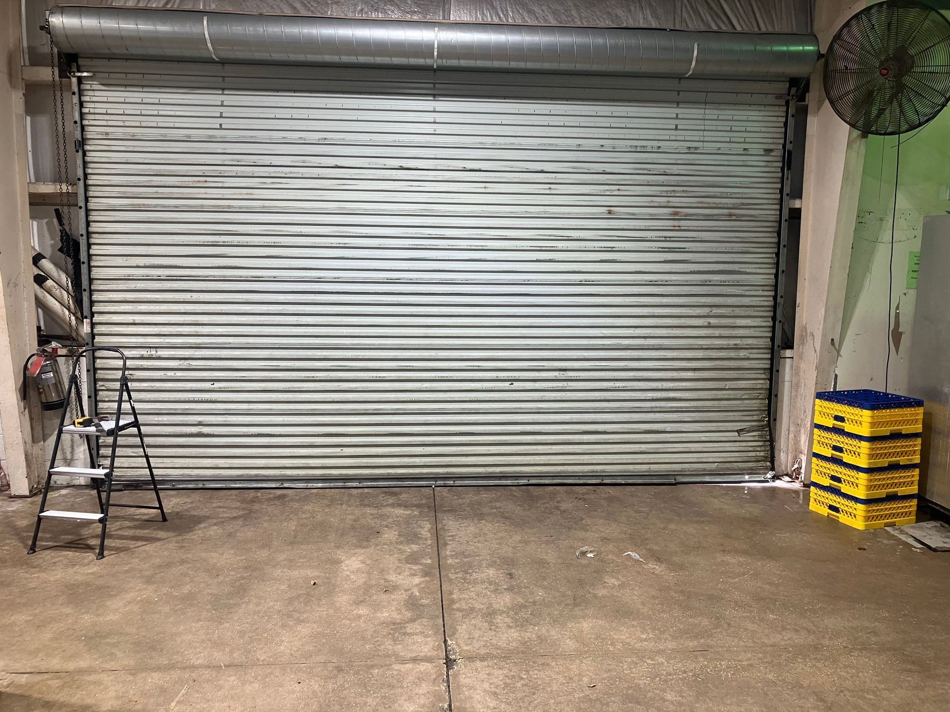 Closed metal roll-up garage door with concrete floor and stacked yellow-and-blue crates on the right