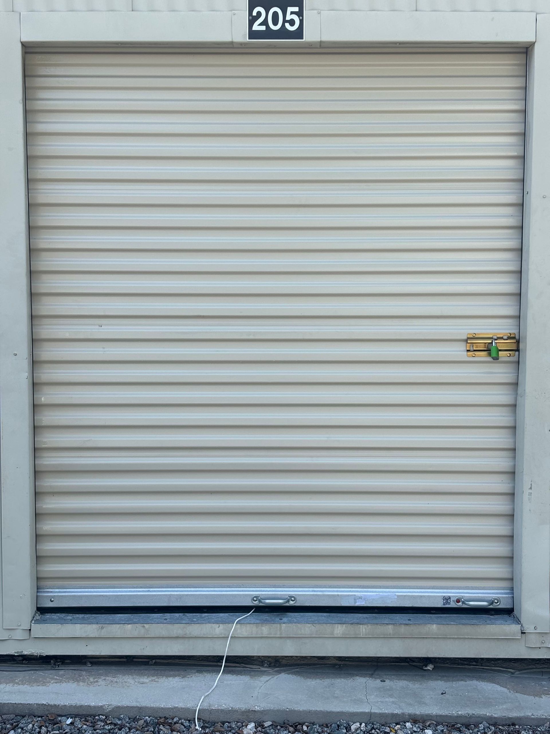 Closed beige roll-up storage door with brass handle and unit number 205 above it