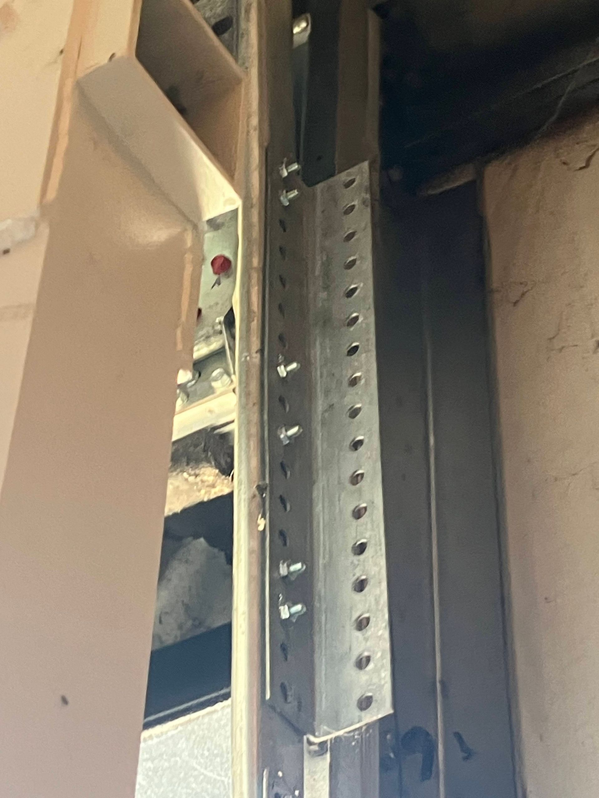 Metal door hardware with a perforated steel bracket and beige panel in a narrow interior space
