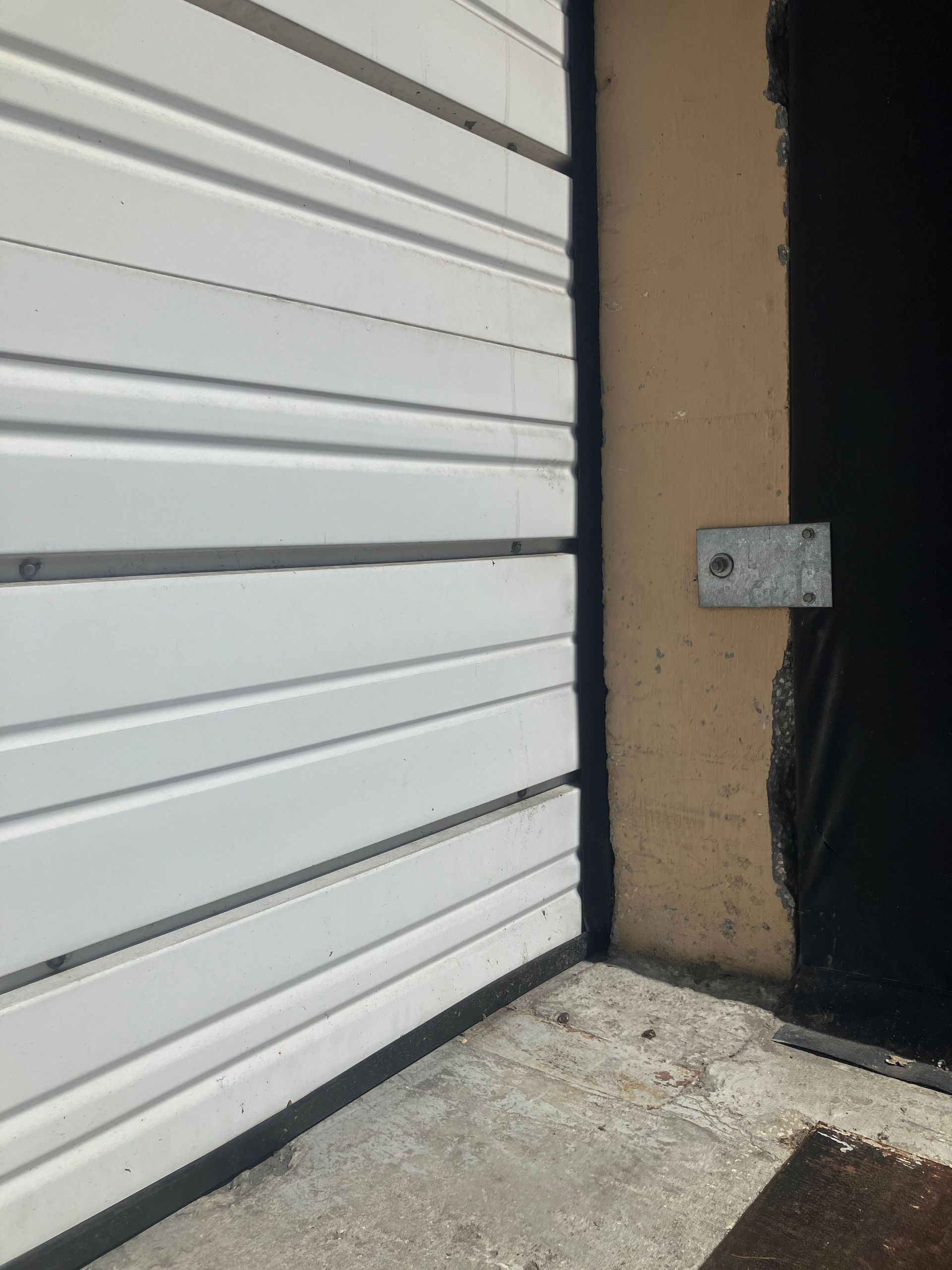 White metal door beside a tan wall with a small mounted plate and concrete floor below