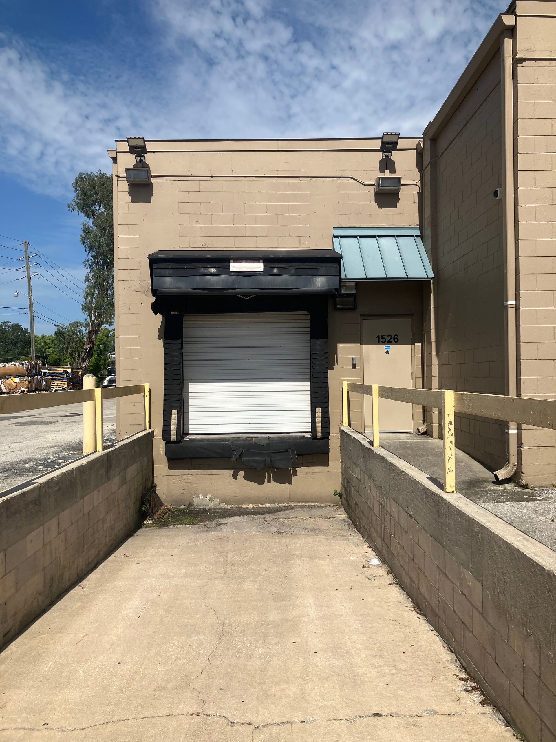 Loading dock with a closed white roll-up door and concrete ramp between beige warehouse walls.
