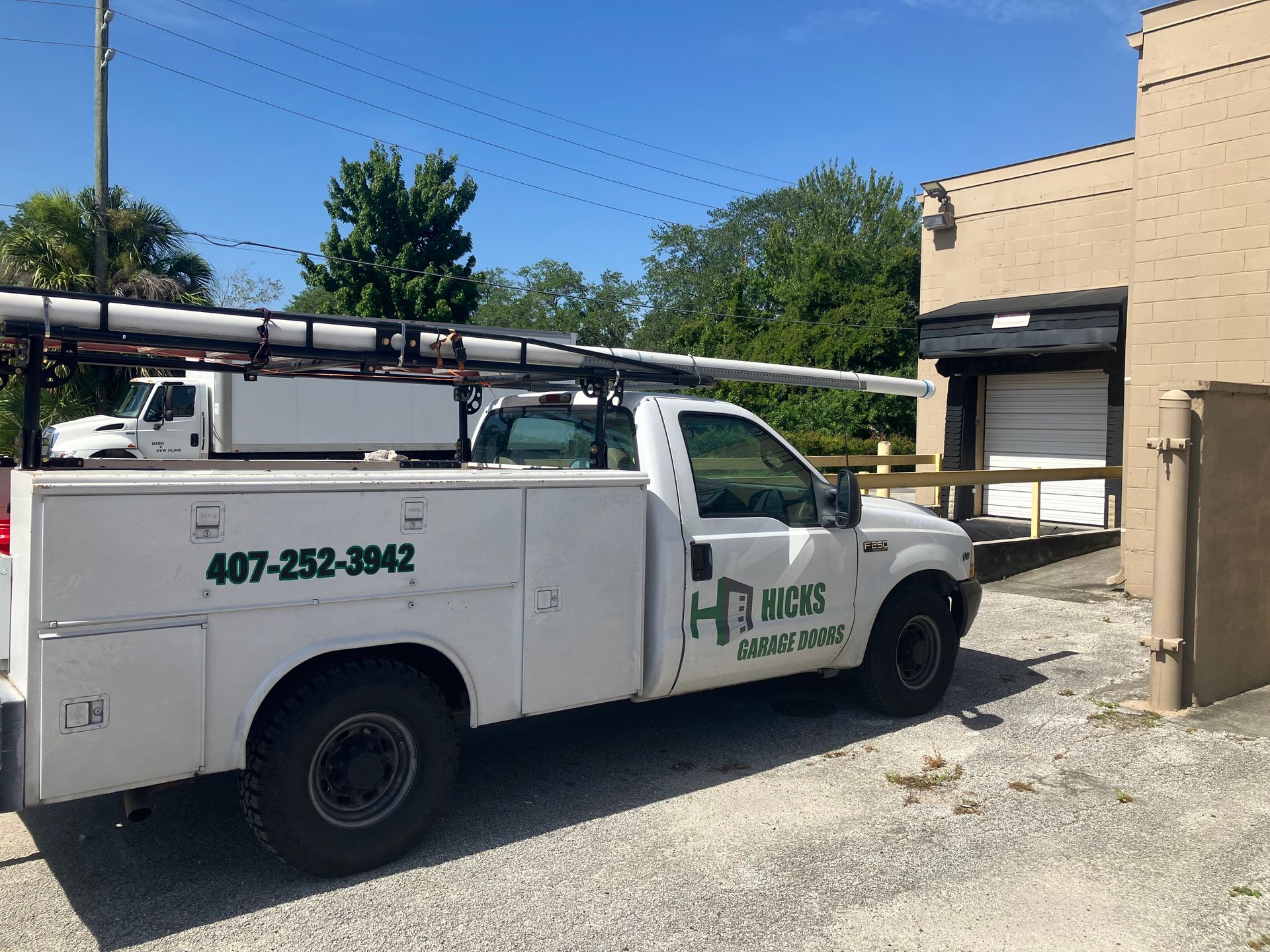 White utility truck parked beside a beige building in a gravel lot on a sunny day