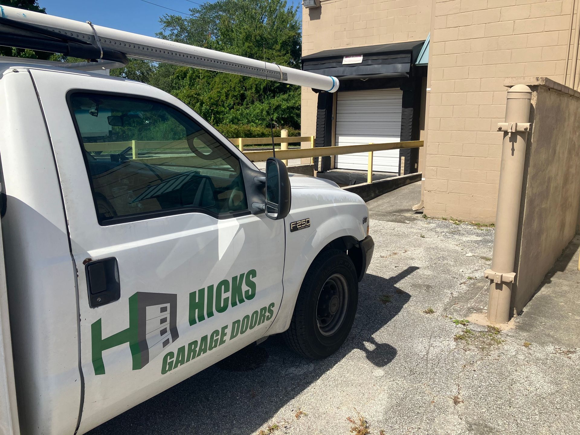 White Hicks Garage Door truck parked beside a building near a garage door.