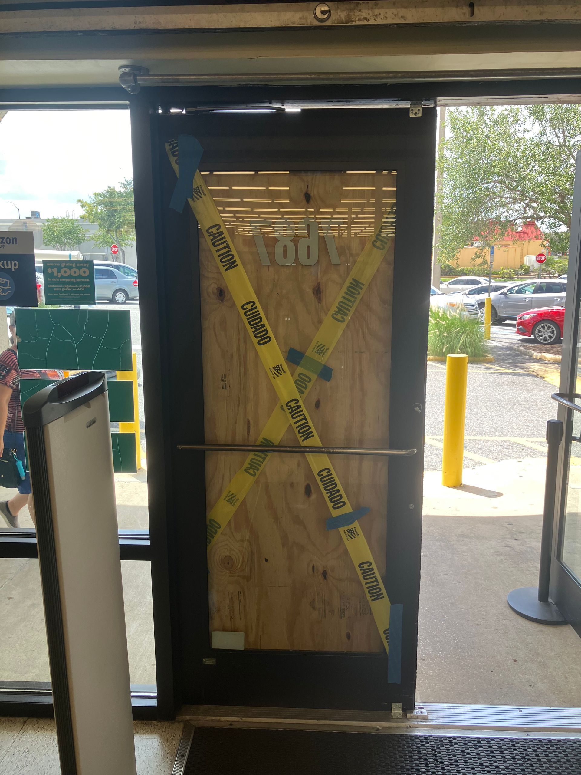 Plywood-covered store entrance with yellow caution tape and black door frame under a covered walkway