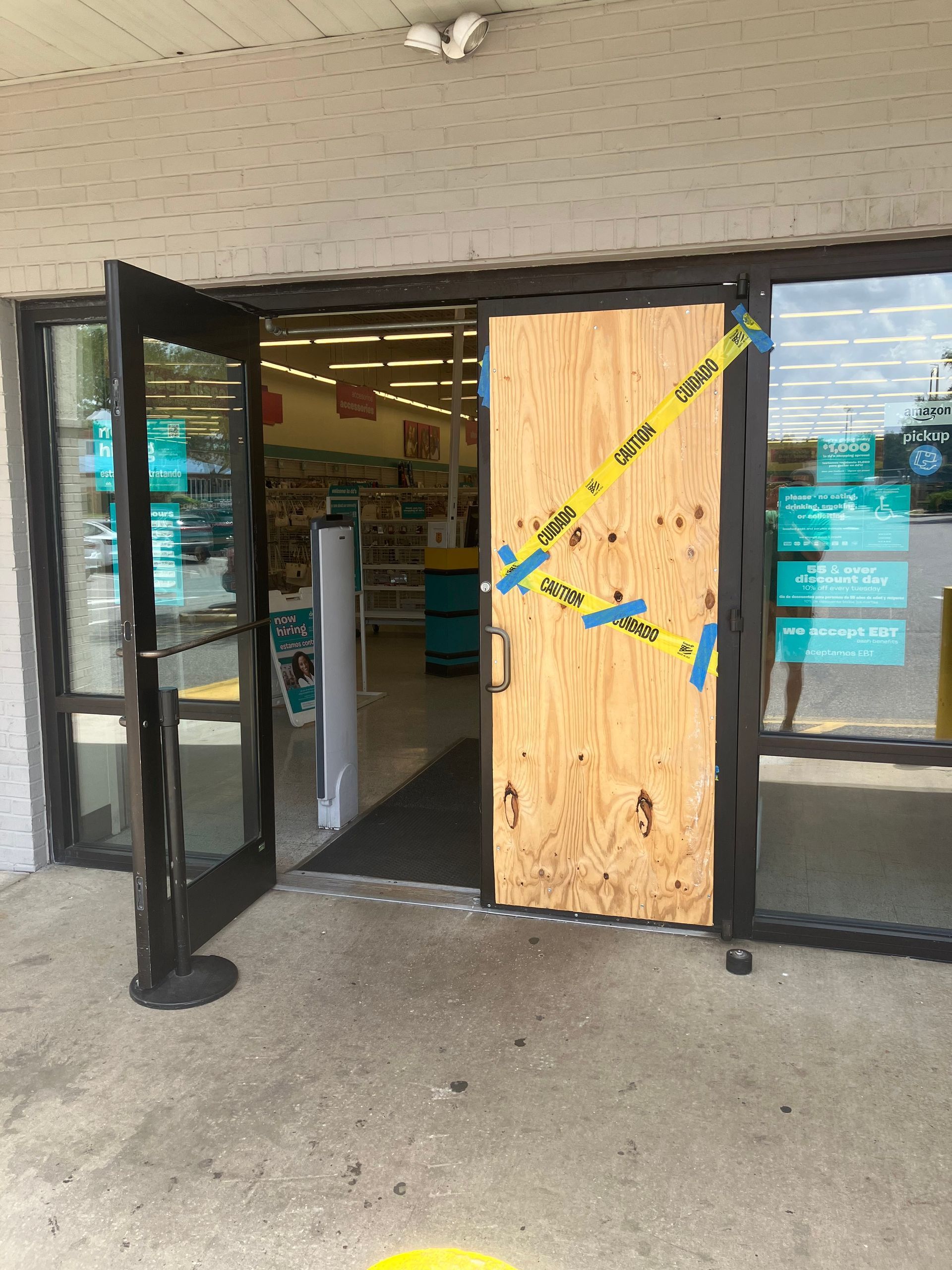 Storefront entrance boarded up with plywood and open glass doors on either side