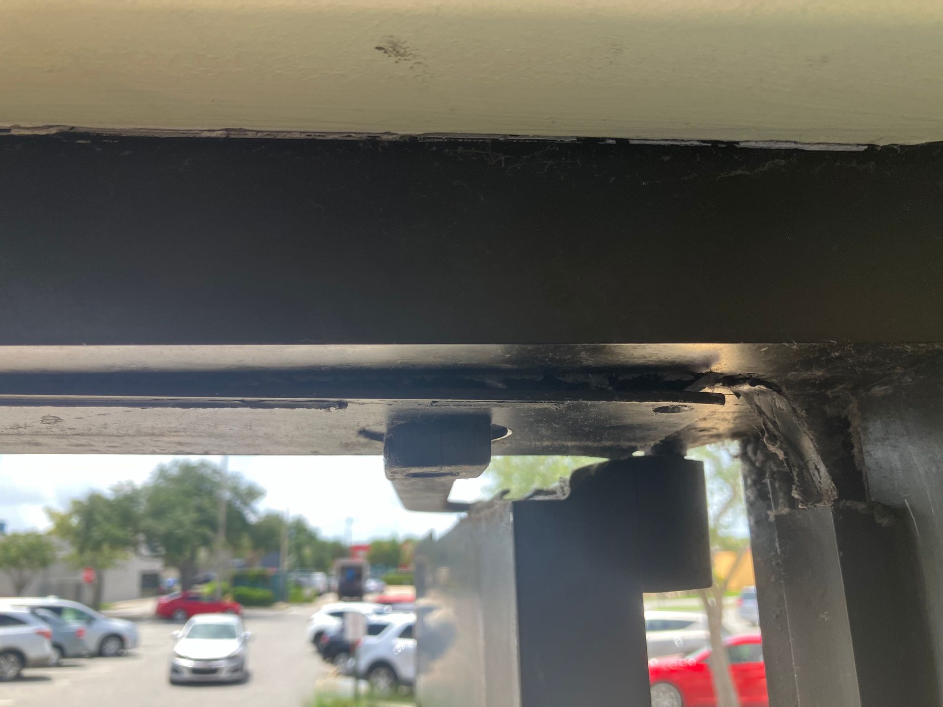 Close-up of a metal bracket and bolt under a ceiling, with a parking lot blurred in the background