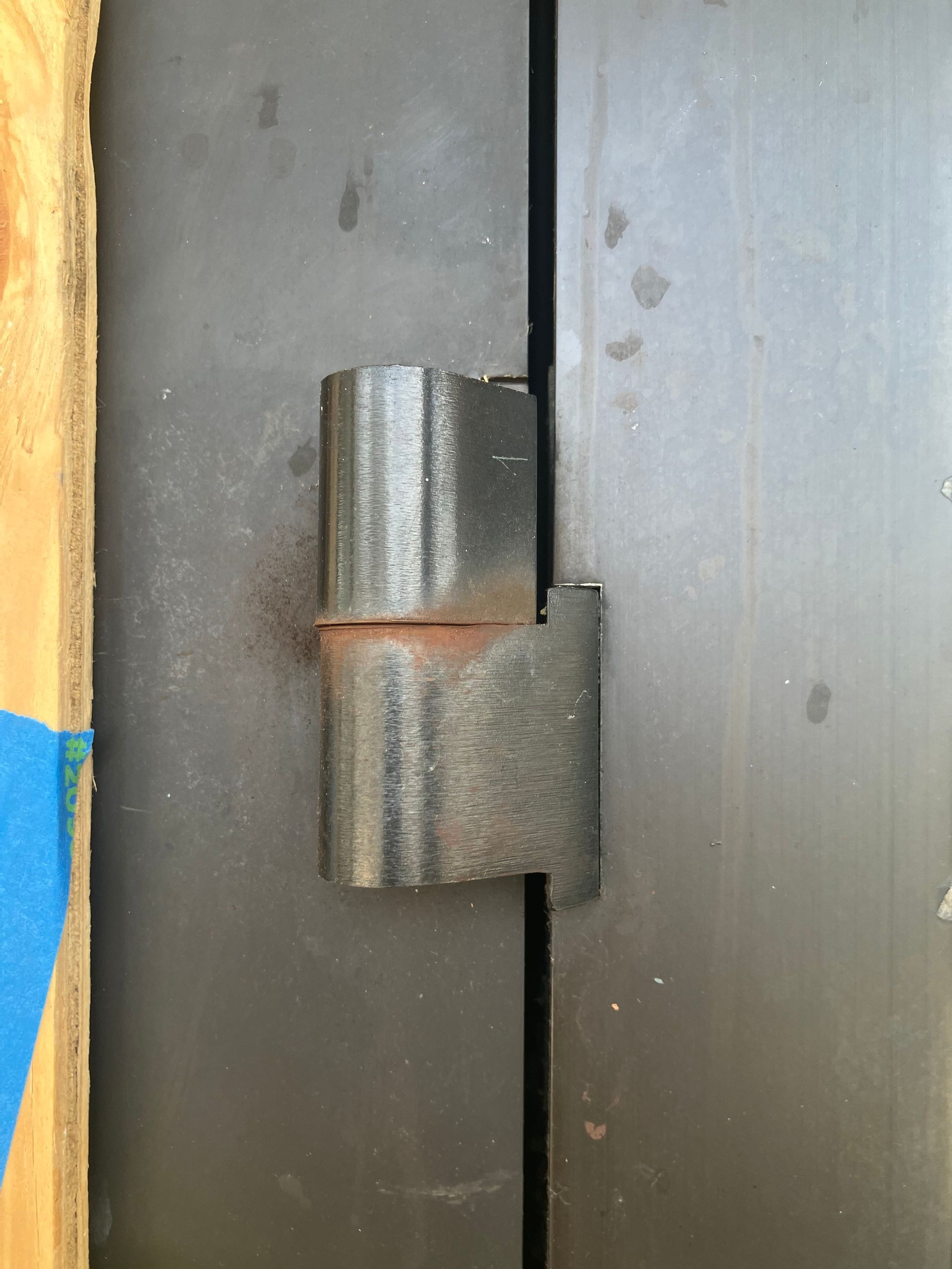 Close-up of a metal door hinge on a gray cabinet or door panel.
