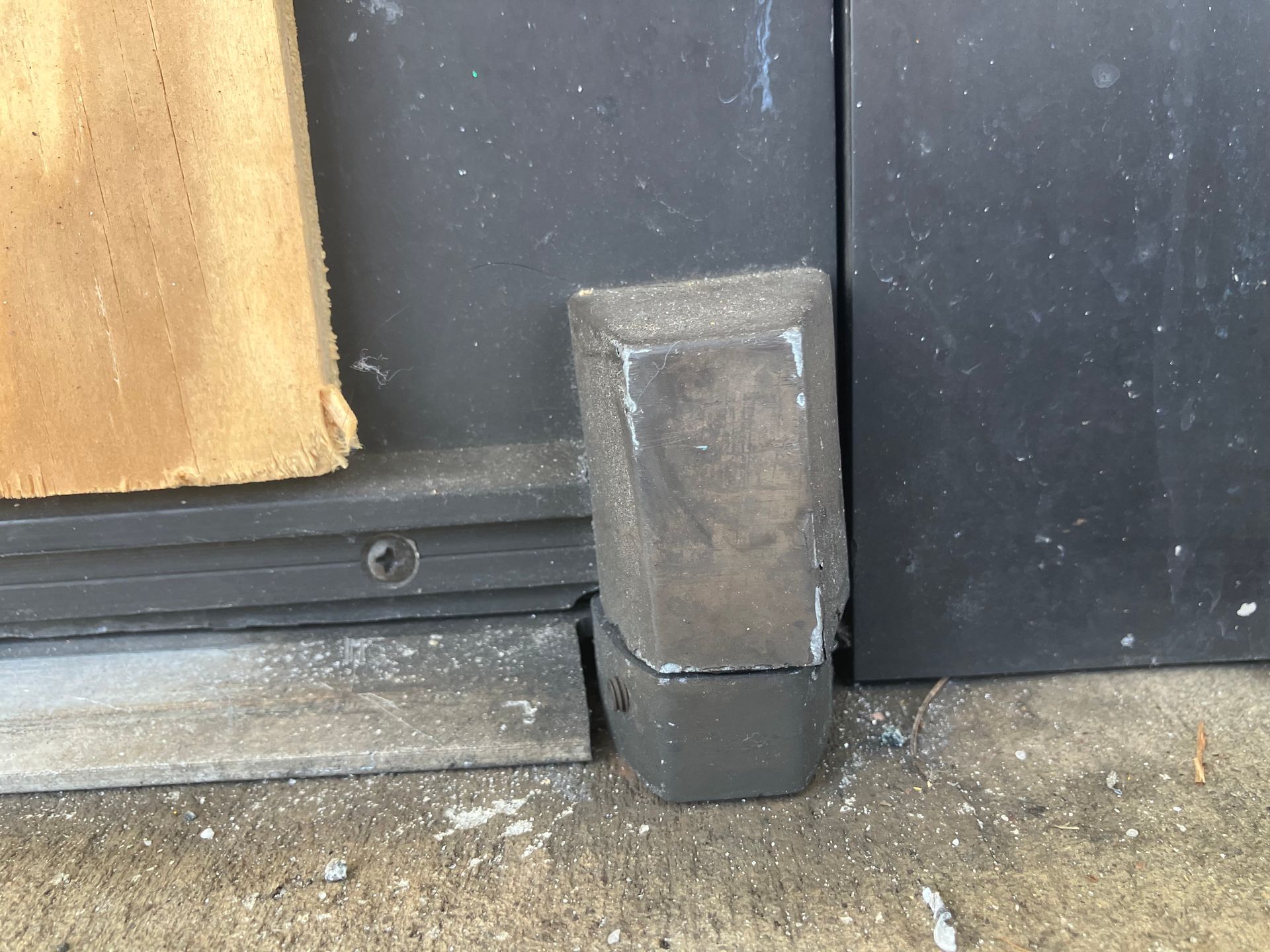 Close-up of a black door’s bottom corner with a rubber threshold stopper beside a wooden panel.
