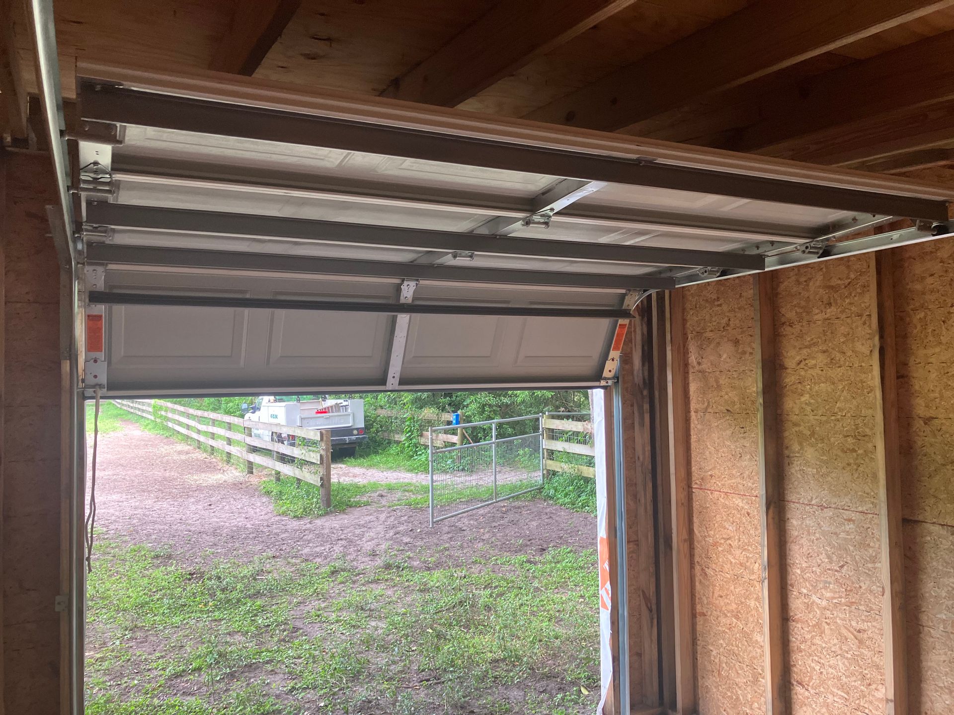 Open garage doorway framing a gravel driveway, green yard, and white fence outside.