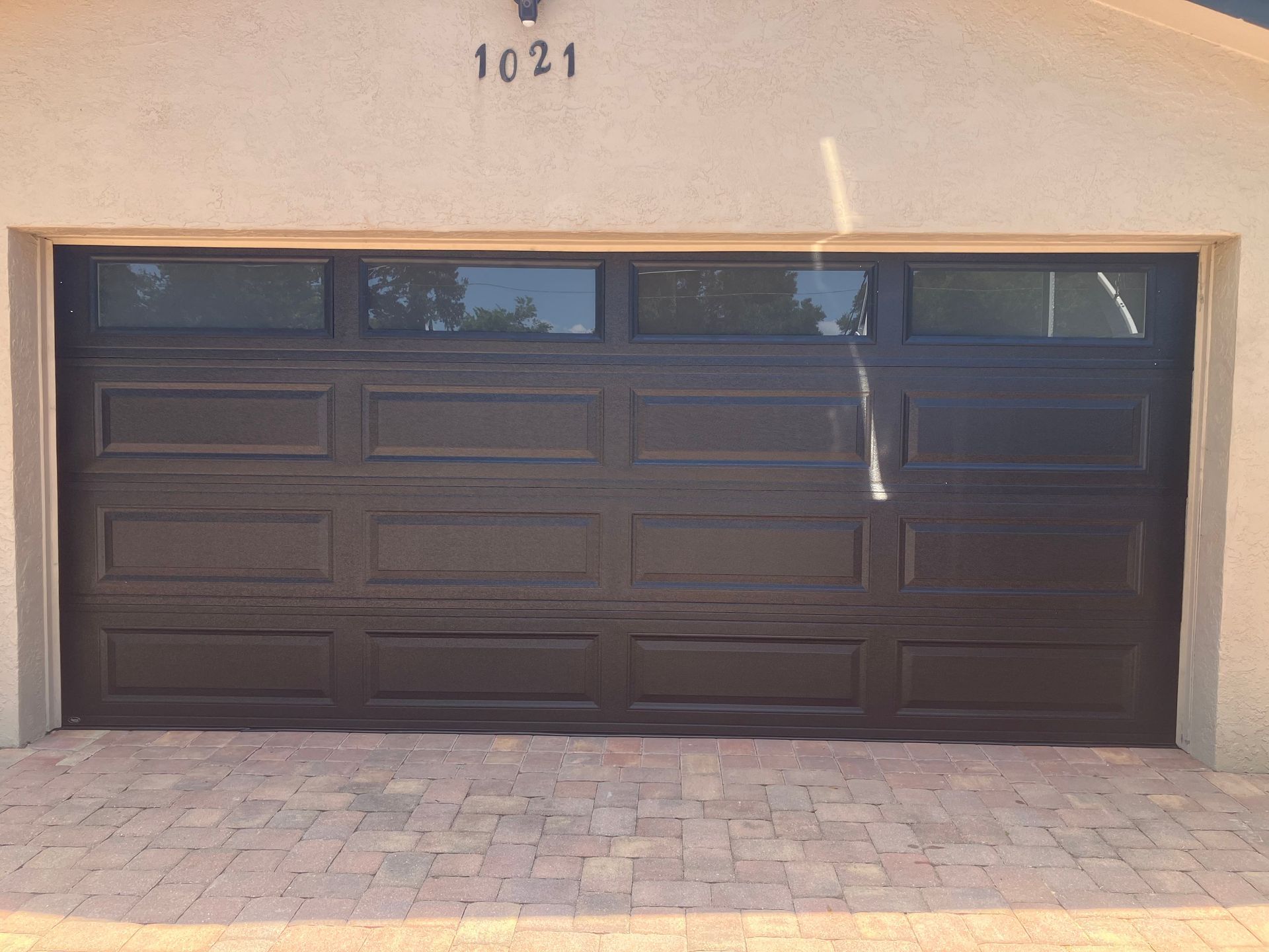 Closed dark brown garage door on a beige house with the number 1021 above it.