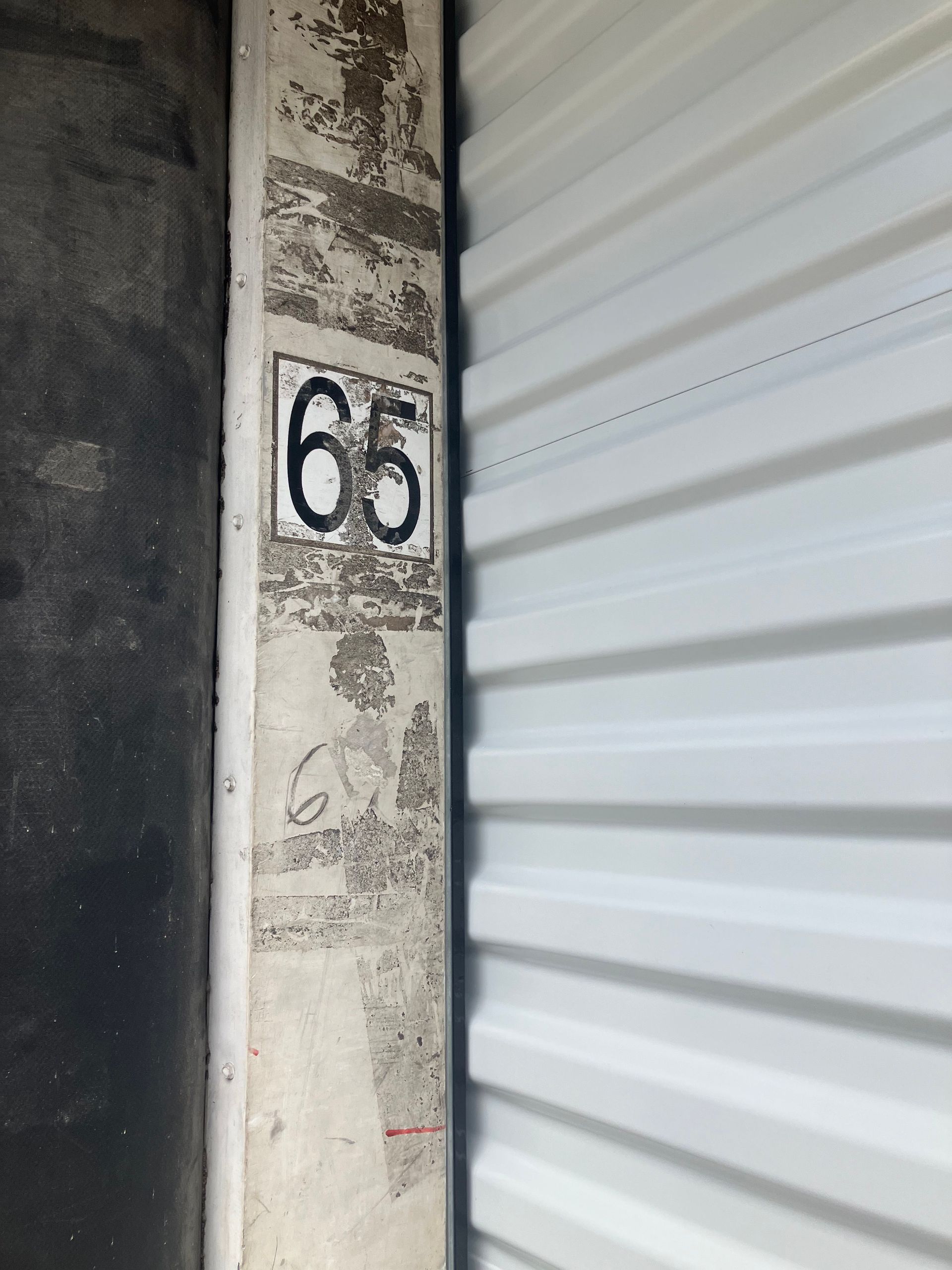 Weathered concrete pillar with the number 65 beside a white corrugated metal door