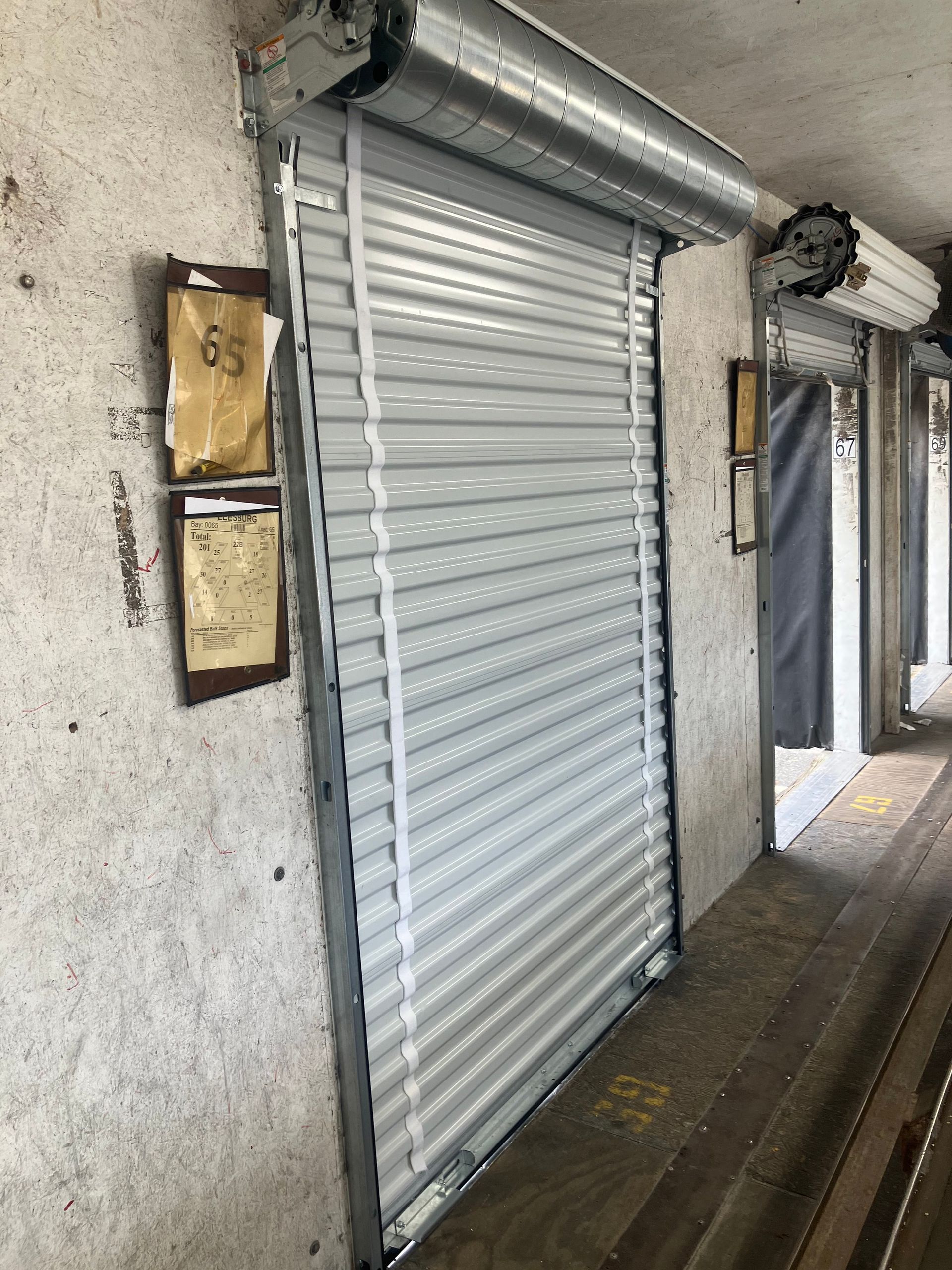 Closed white roll-up door beside mailboxes in a narrow outdoor walkway.