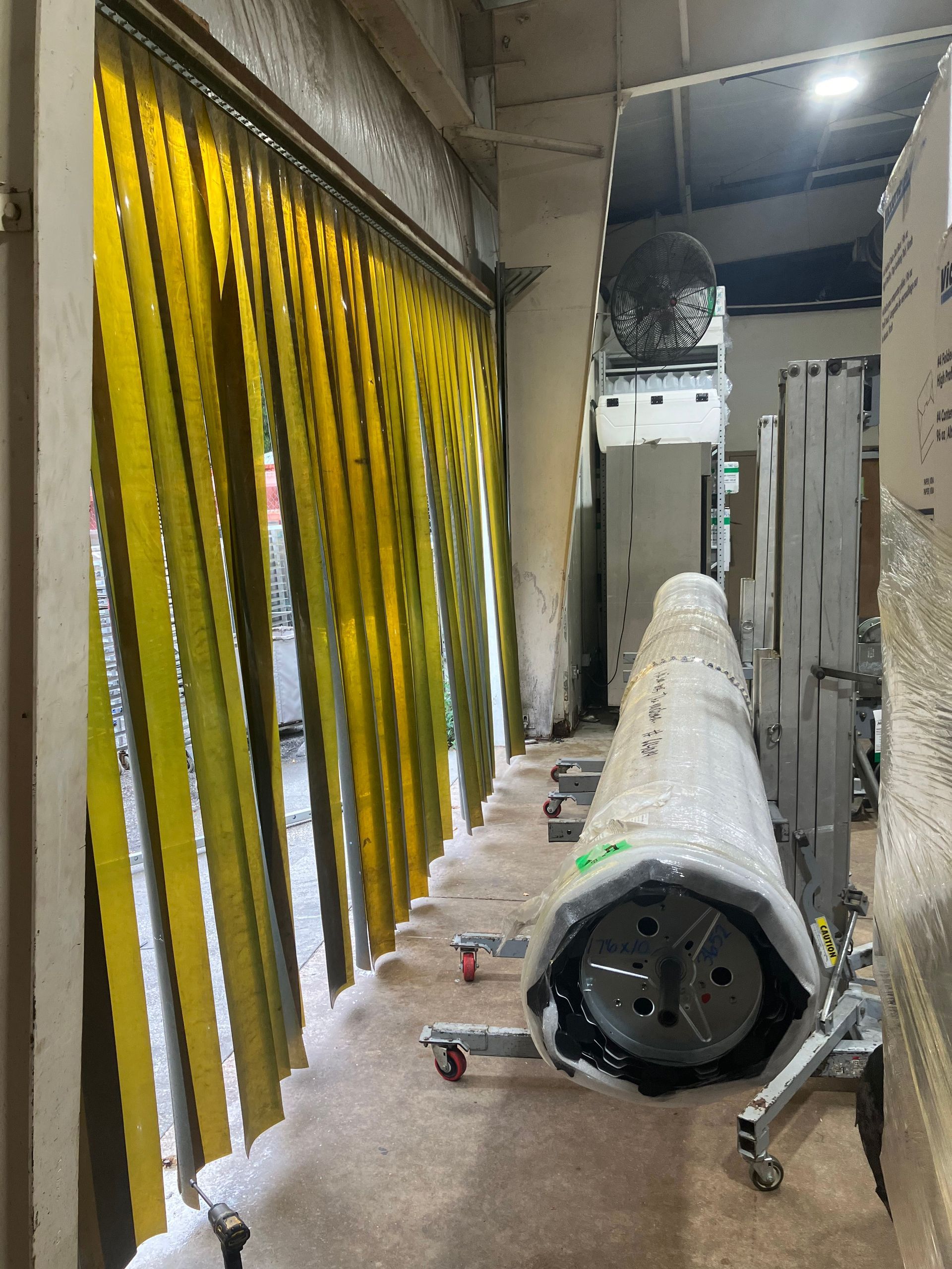 Construction corridor with yellow hanging barriers and a rolled white material on the floor