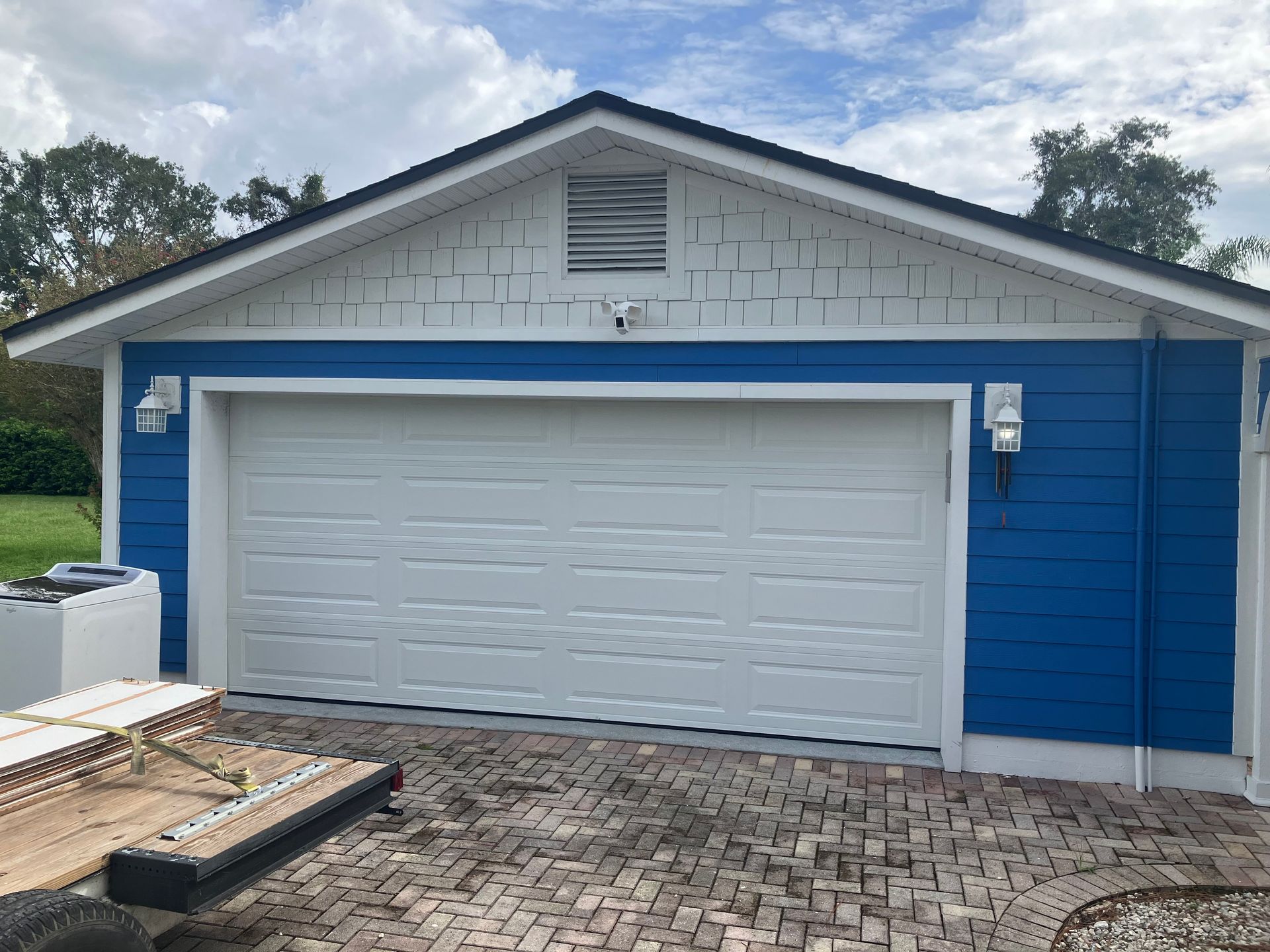 Blue garage with white door and trim, brick driveway, and cloudy sky above.