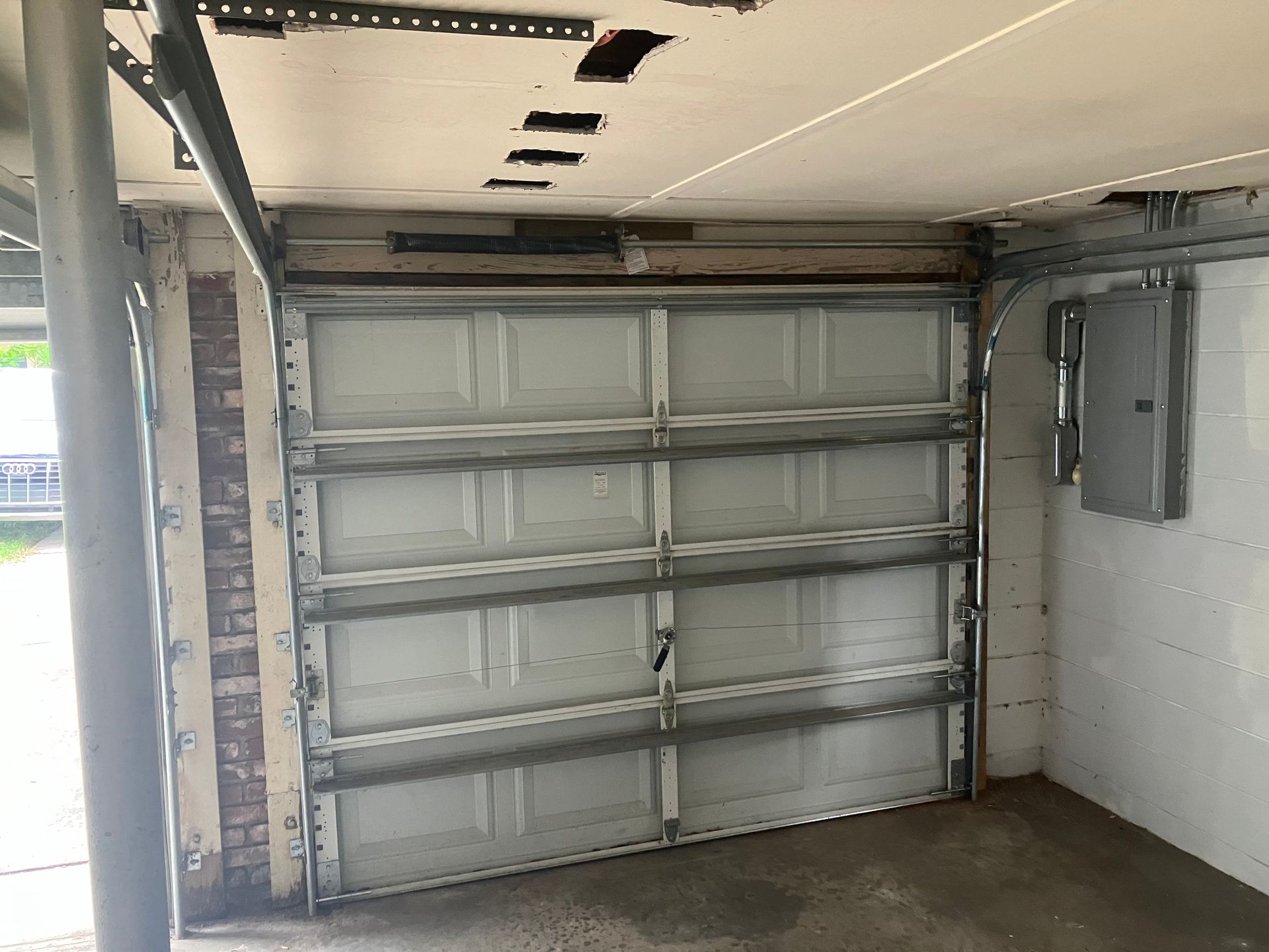 Open garage interior with a closed white sectional garage door and exposed ceiling framing.
