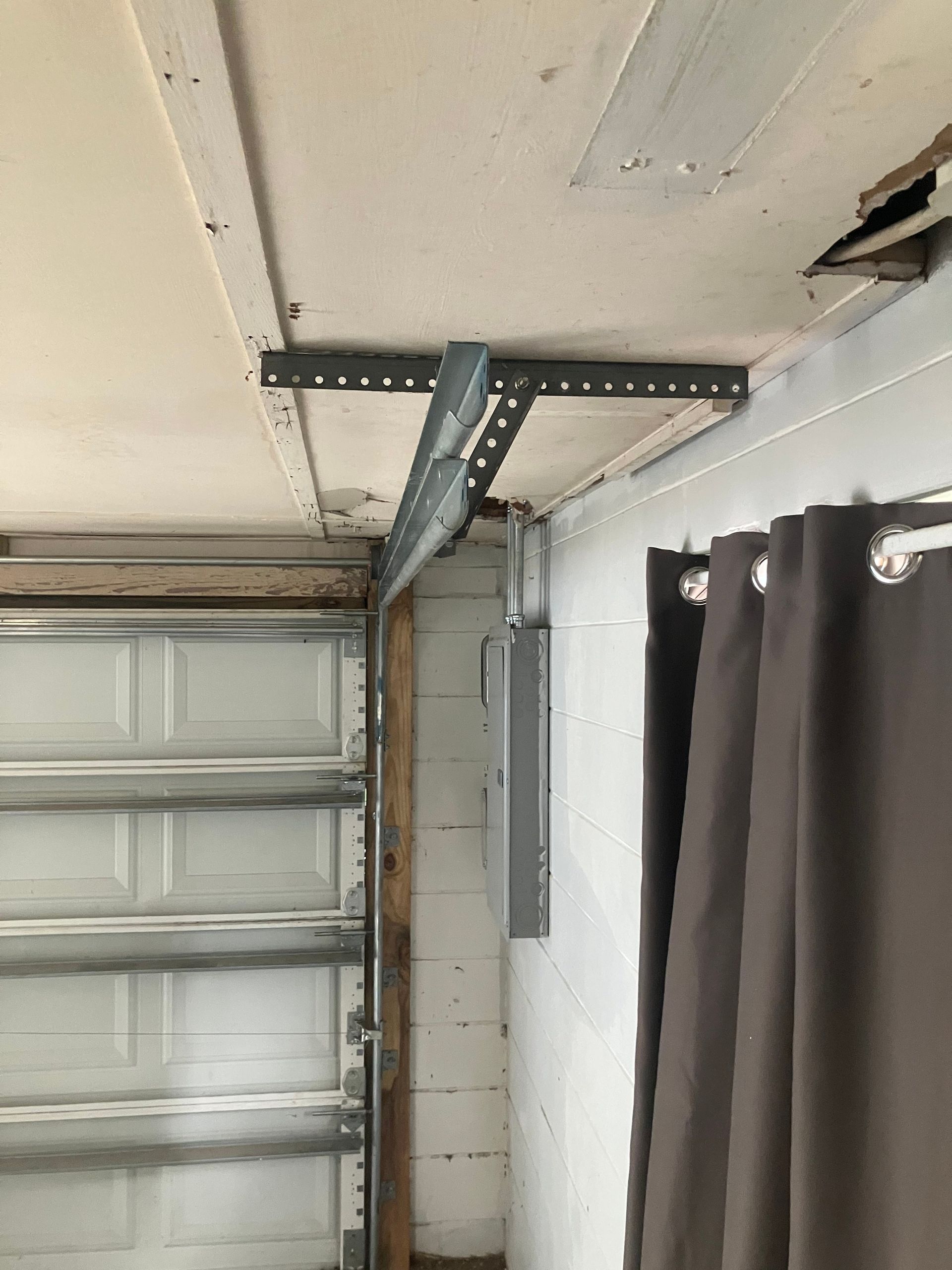 Garage ceiling with garage door track, metal support bracket, and hanging dark curtain.