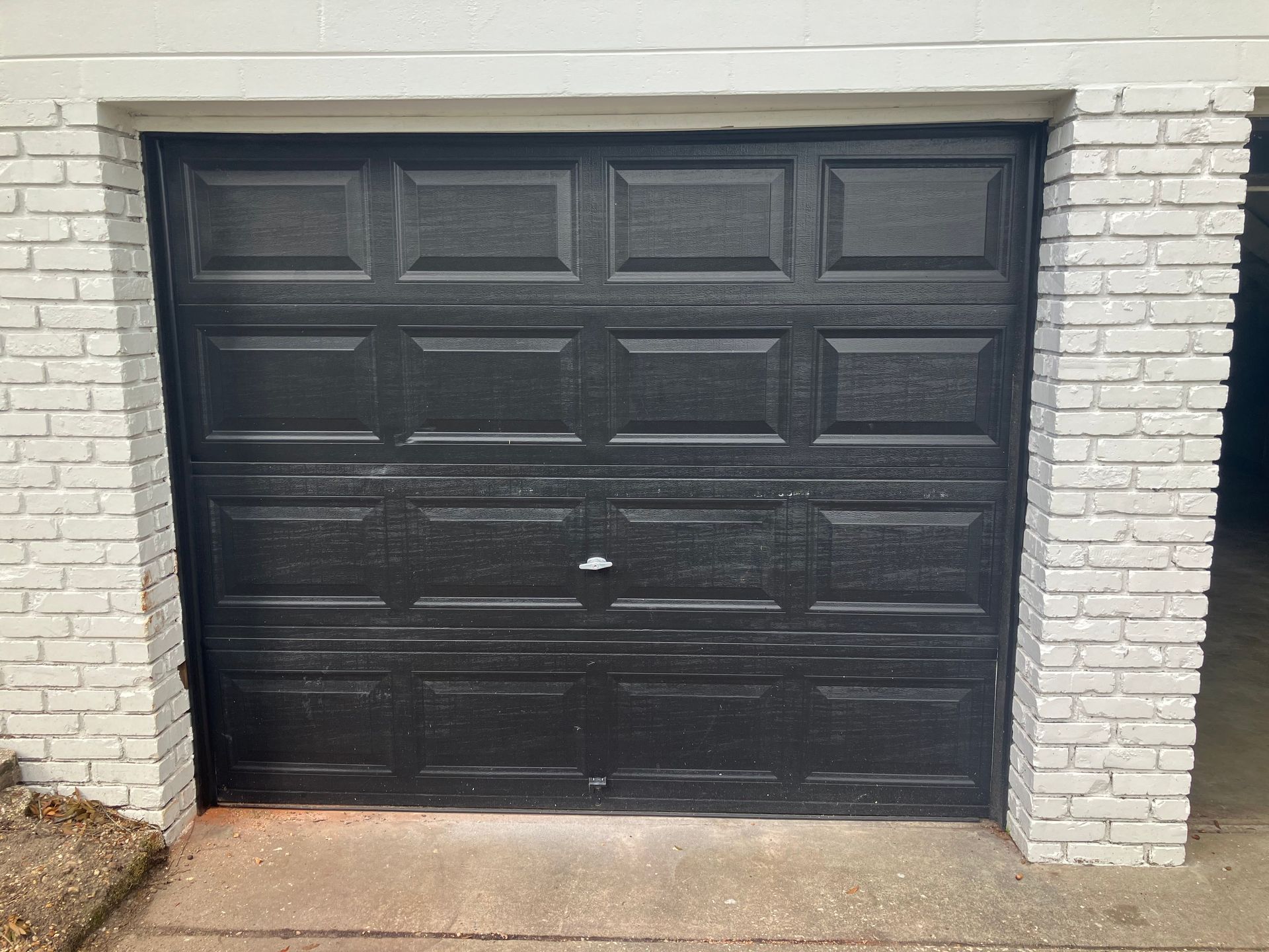 Black garage door set in a white brick exterior wall.