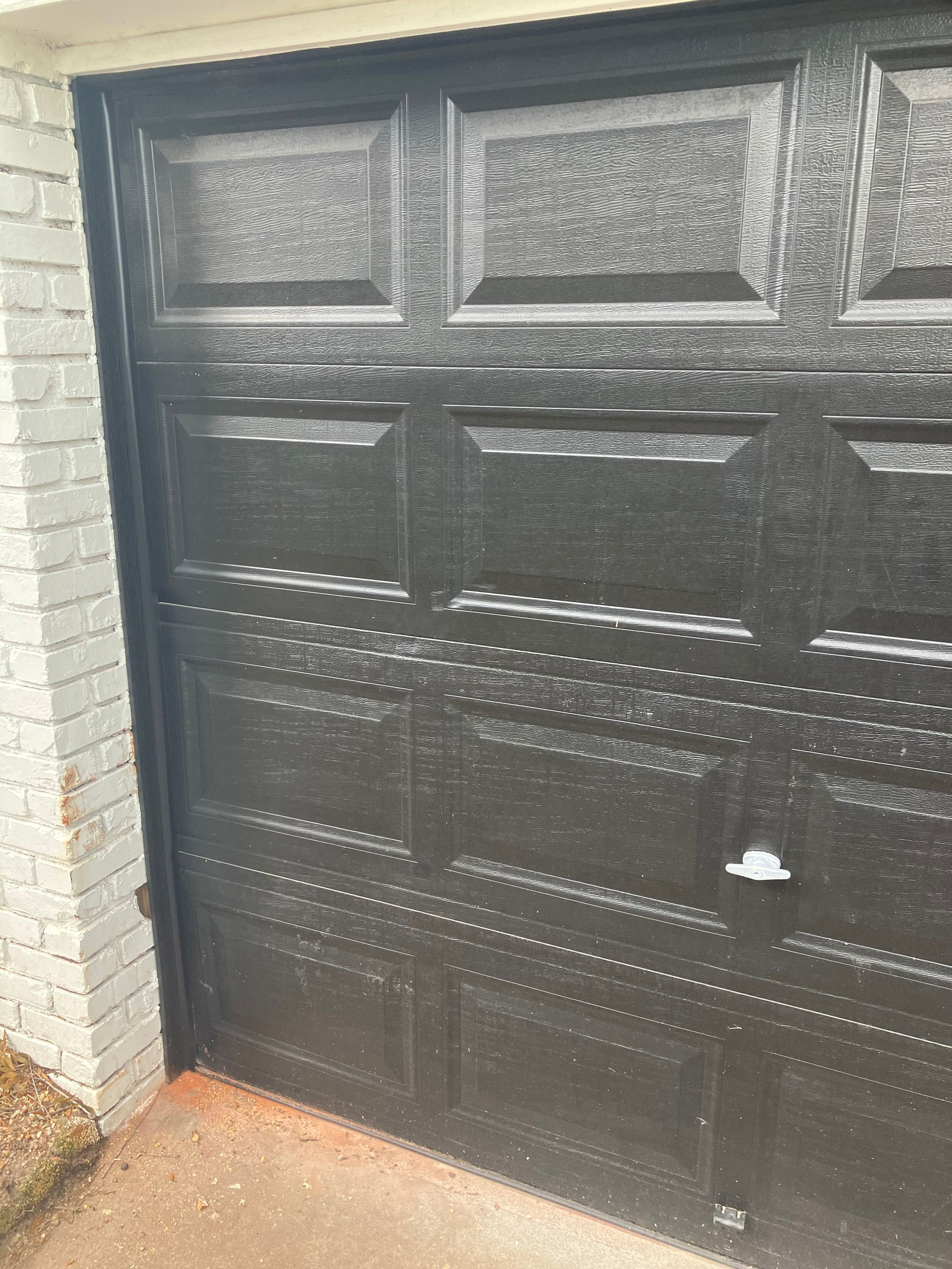 Black garage door with a white brick wall and concrete driveway beside it