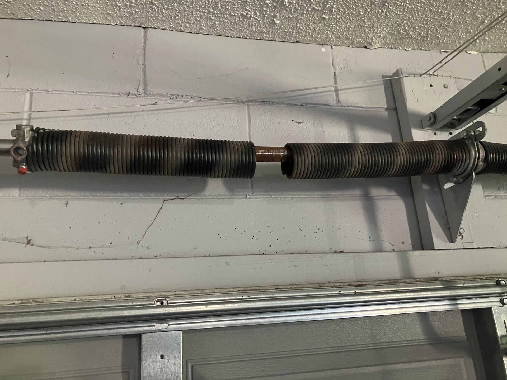 Garage door torsion spring mounted above a white cinder block wall.