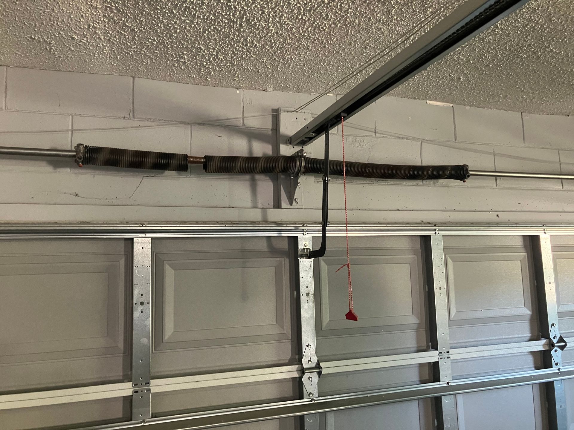 Garage interior with a closed sectional door, ceiling opener rail, and hanging red pull cord