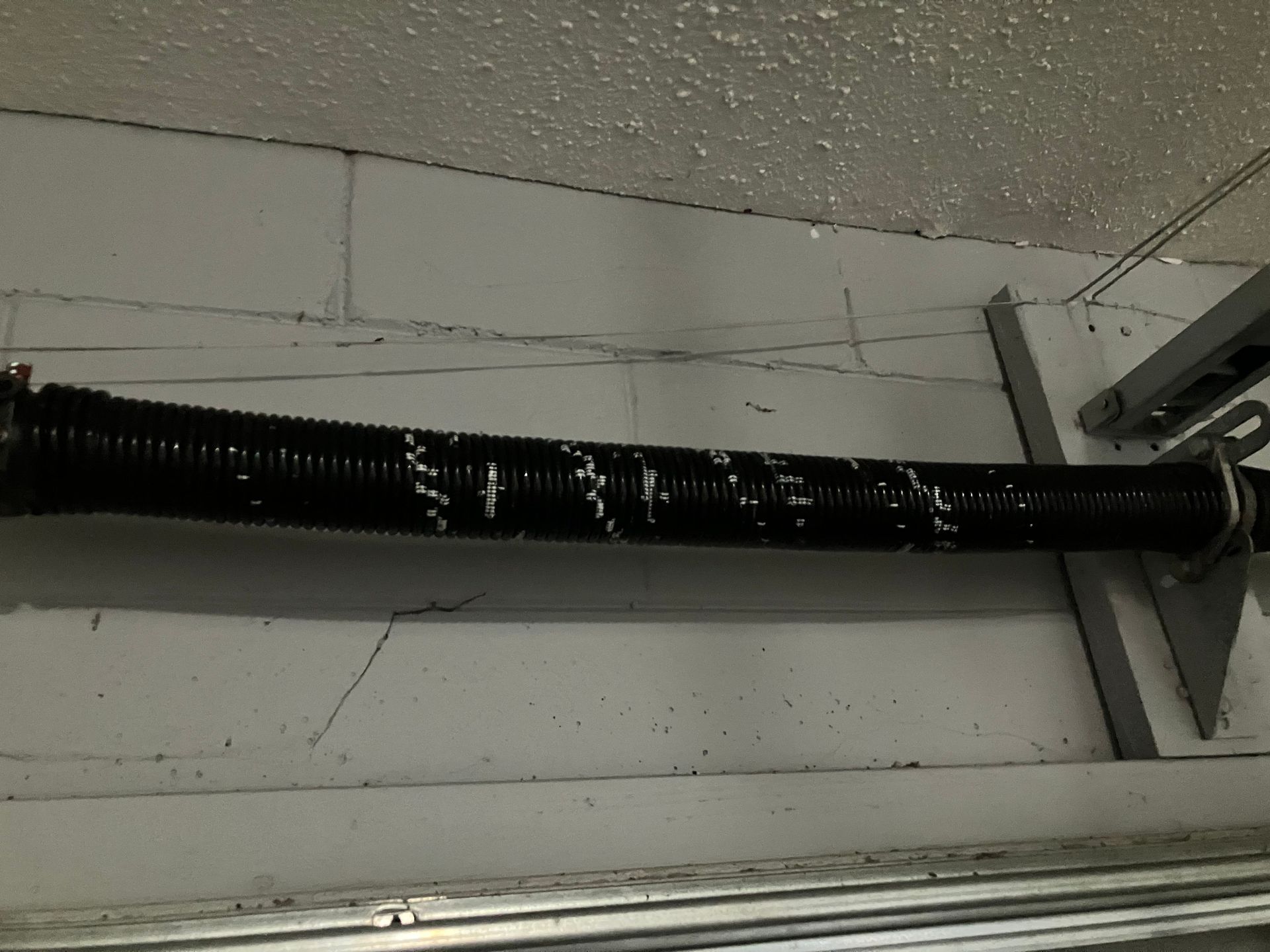 Black corrugated pipe mounted horizontally on a white wall near the ceiling