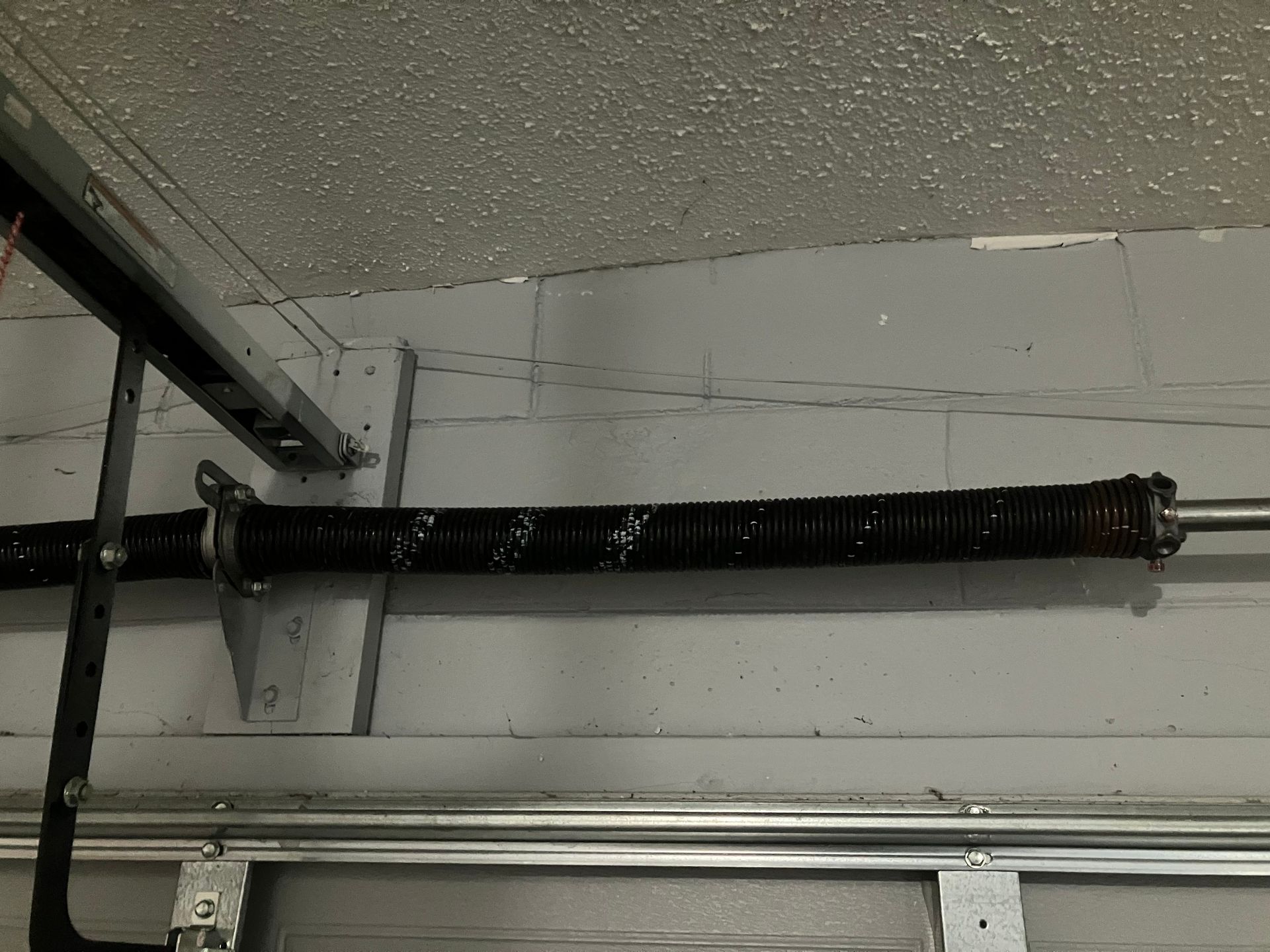 Black insulated pipe with a red valve along a cinder block wall near the ceiling.