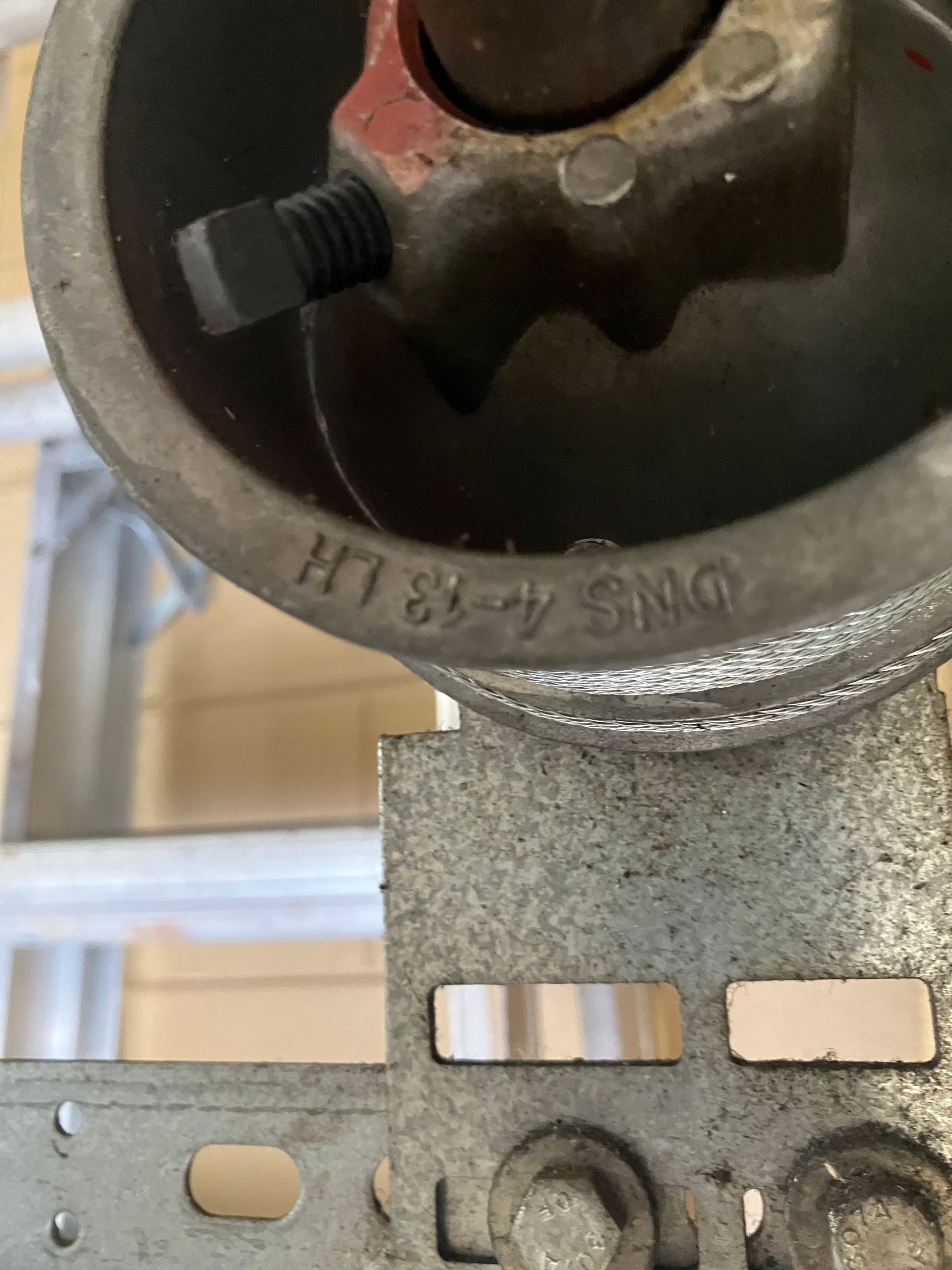 Close-up of a gray metal pipe fitting with a black screw on a perforated metal bracket.