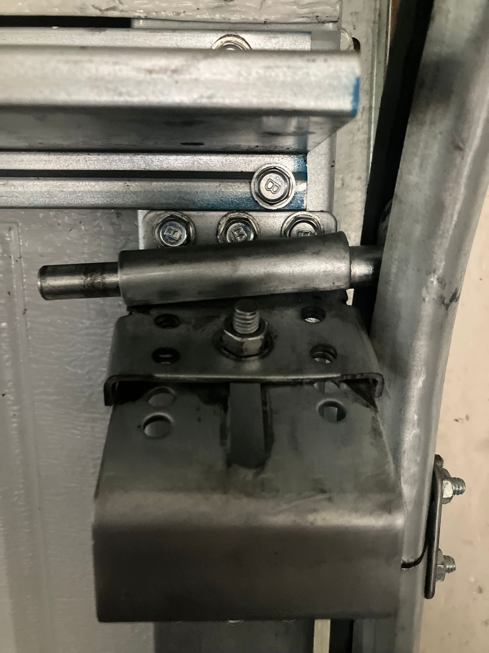 Close-up of a metal hinge and bracket assembly on a gray industrial door or machine panel