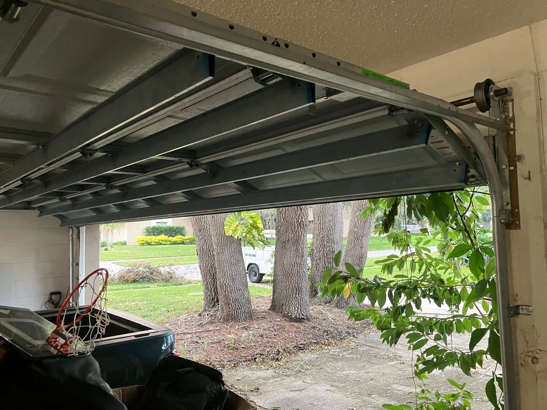 Open garage with overhead door, storage bins, and a view of trees and yard outside.