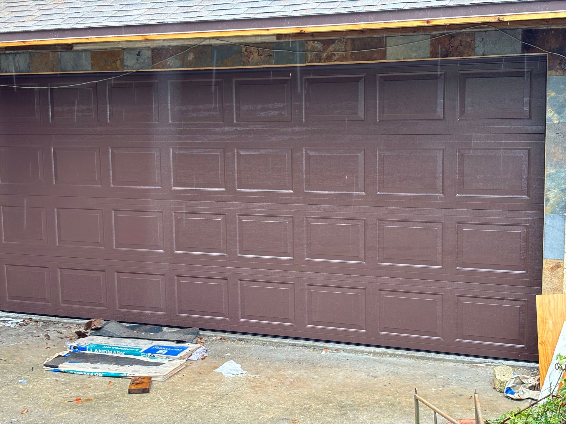 Brown garage door under construction with white trim and debris on the ground