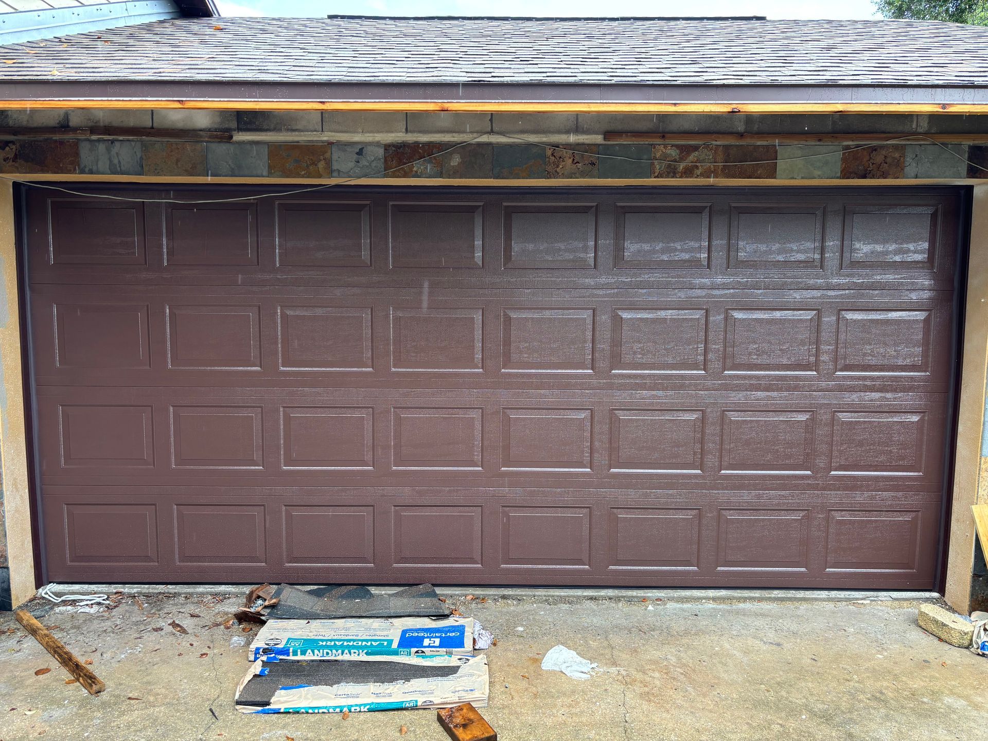 Brown garage door on a house exterior with a package lying on the driveway in front.