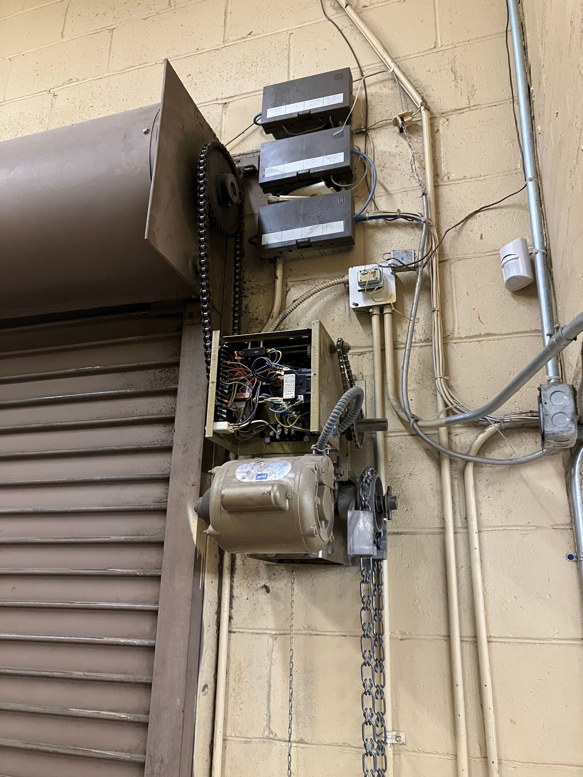 Damaged electrical meter and breaker boxes mounted on an exterior beige wall with exposed wiring