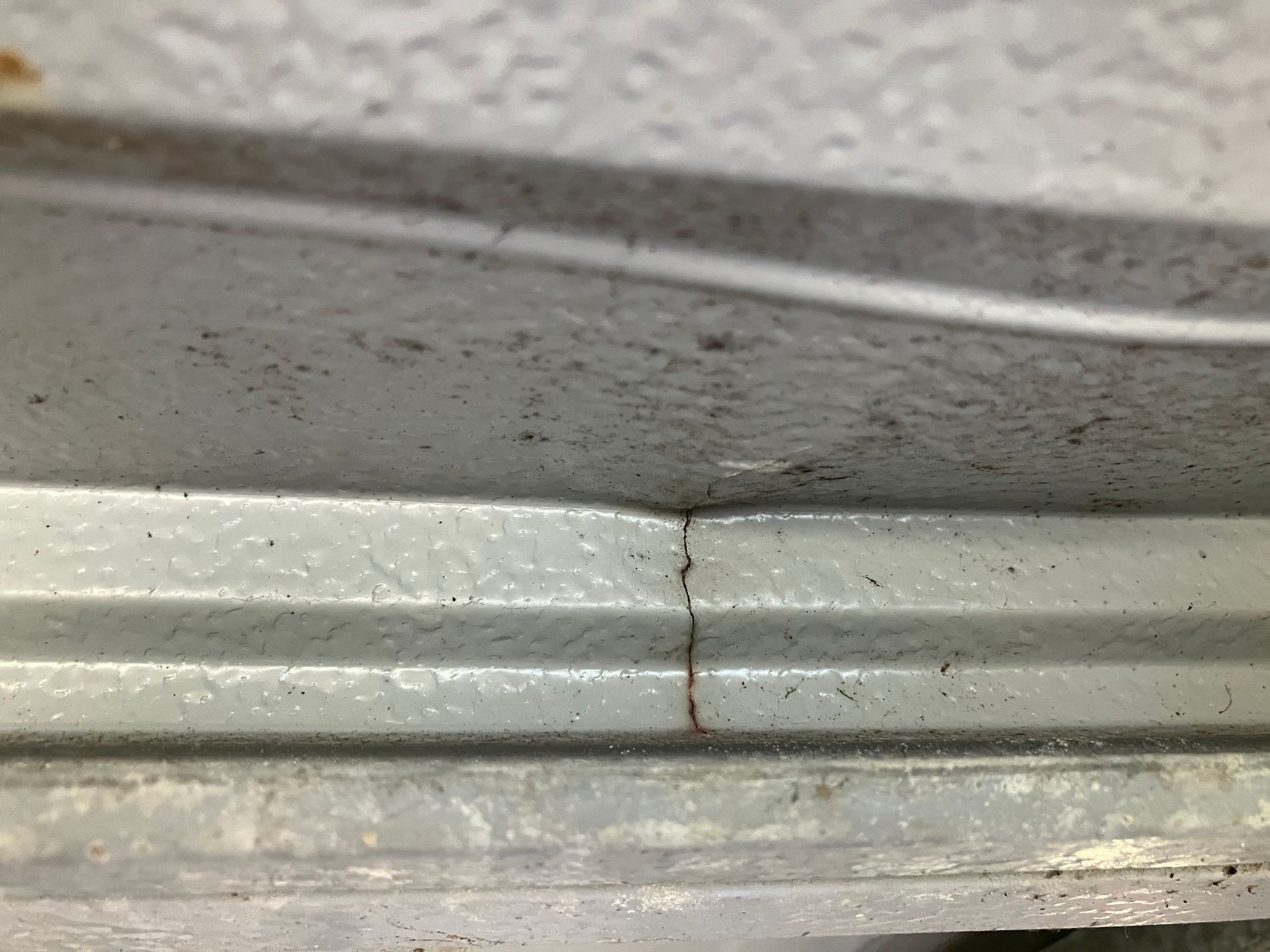 Close-up of a cracked white wall trim or molding with a vertical split and chipped paint.