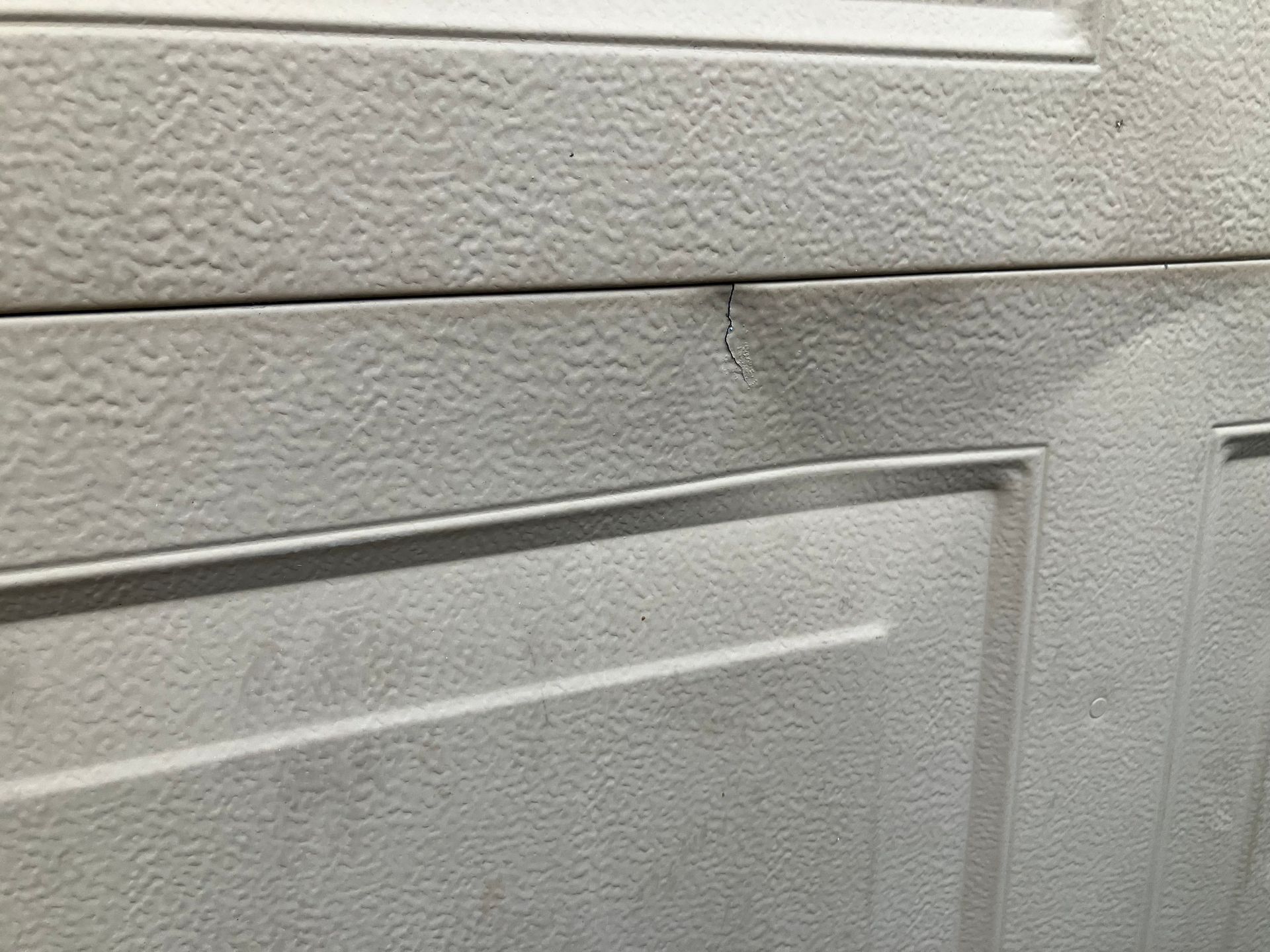 Close-up of a white paneled door or wall with a textured surface and a small scuff mark near the top.