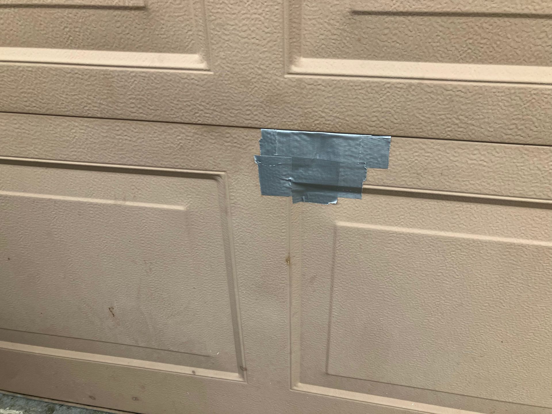 Blue tape securing a crack in a beige paneled wall or garage door.