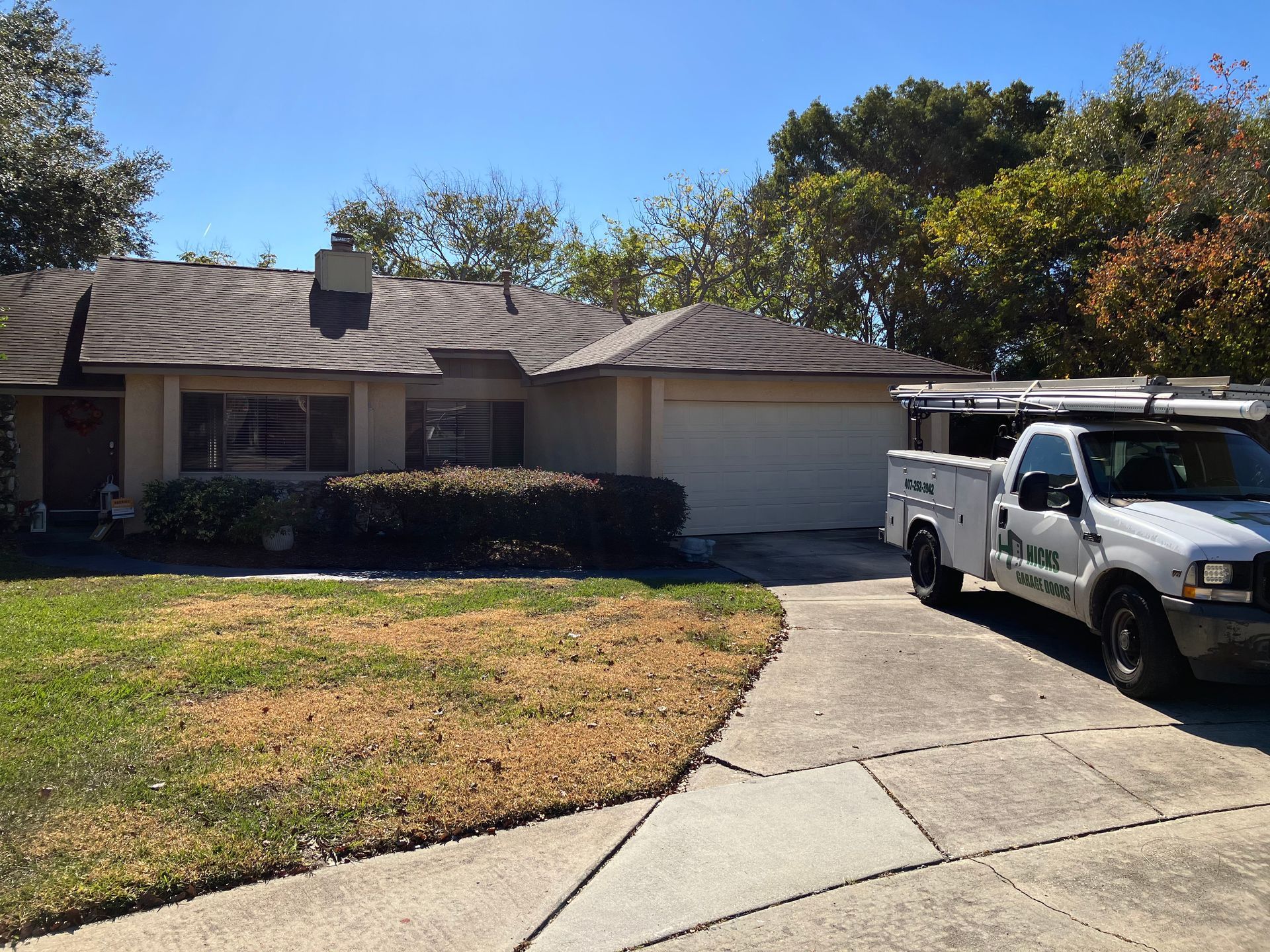 Suburban house with driveway, lawn, and white utility truck parked outside in bright sun